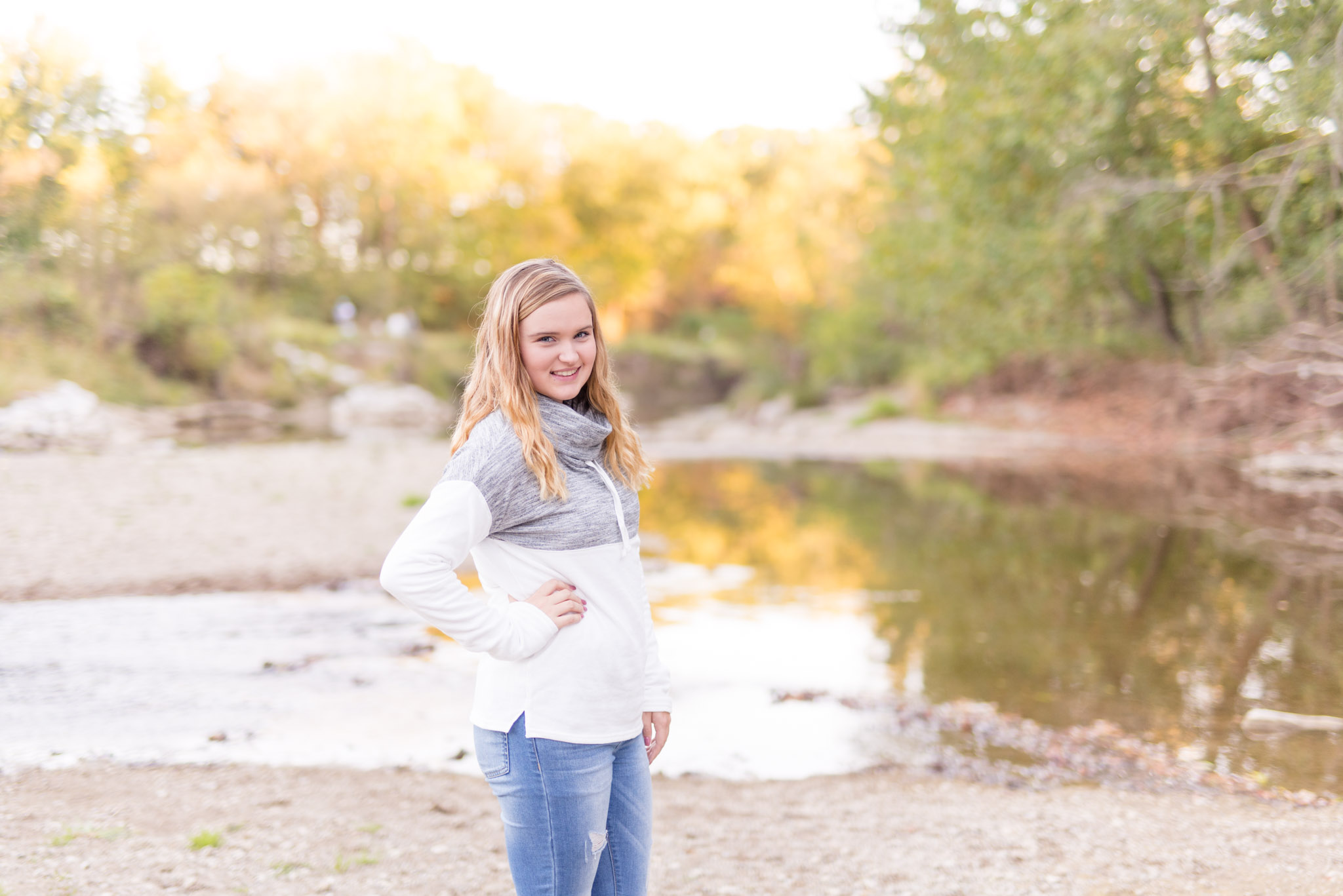 Girl in white sweater stands near river.