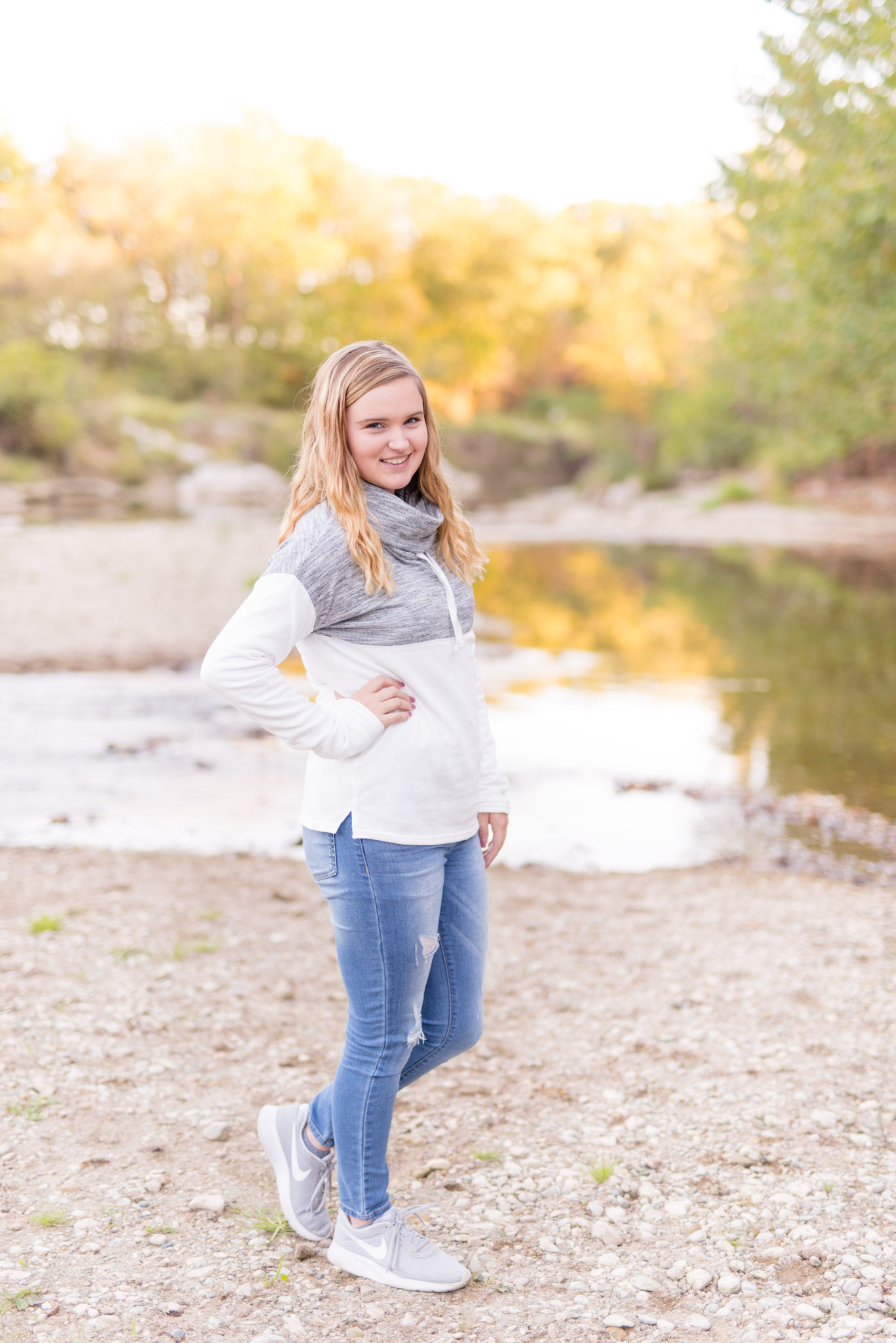 Girl in white sweater stands in front of river.