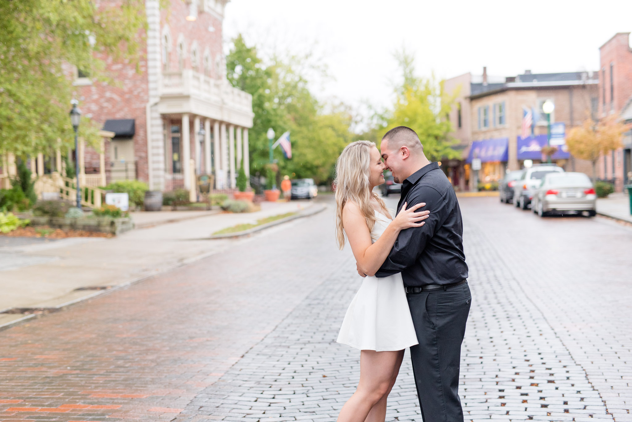Engaged couple kiss on downtown brick street.