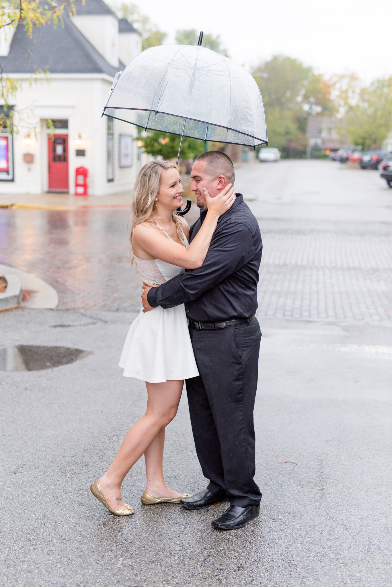 Engaged couple smiles under umbrella in downtown.