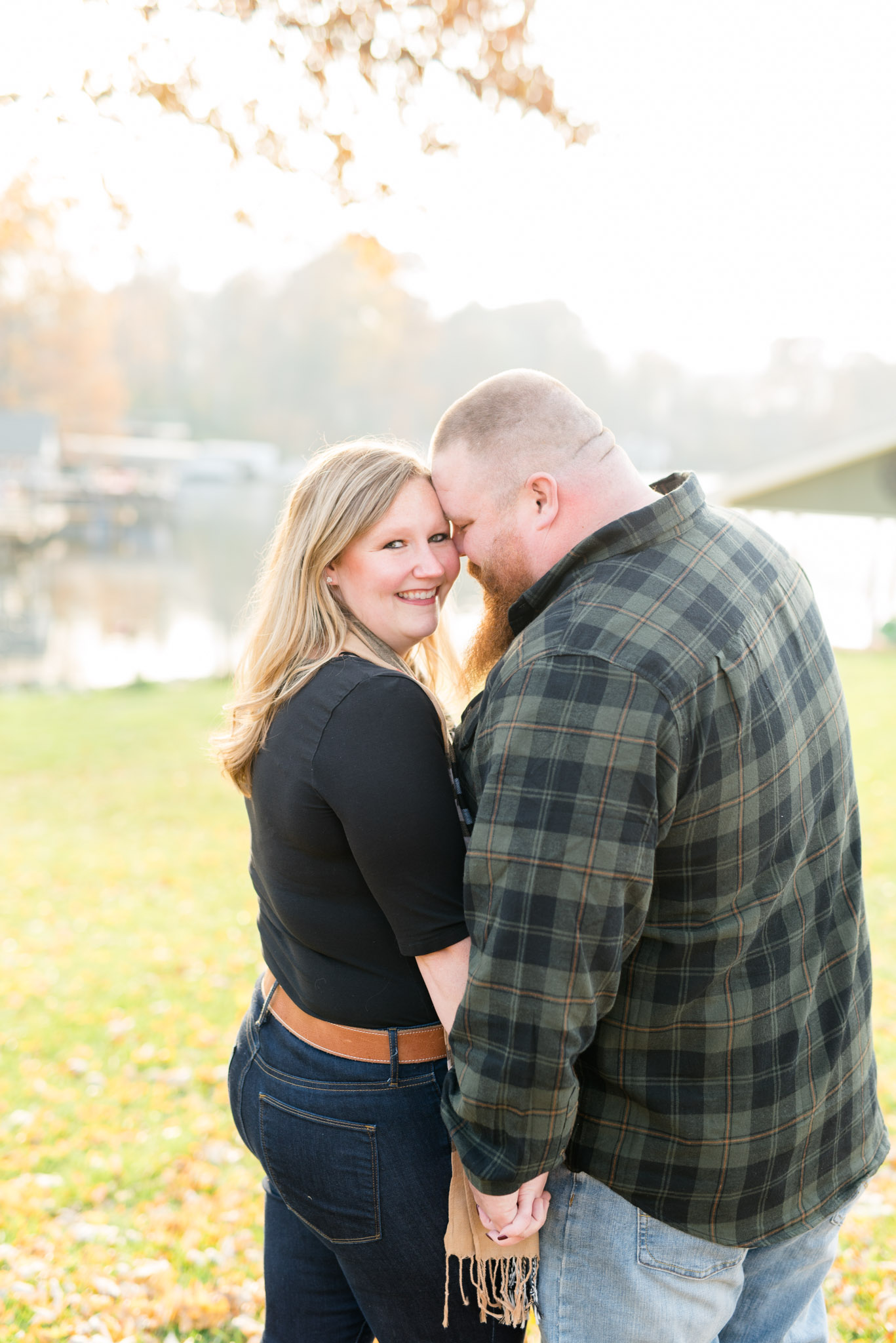 Engaged bride looks at camera while groom smiles at her.