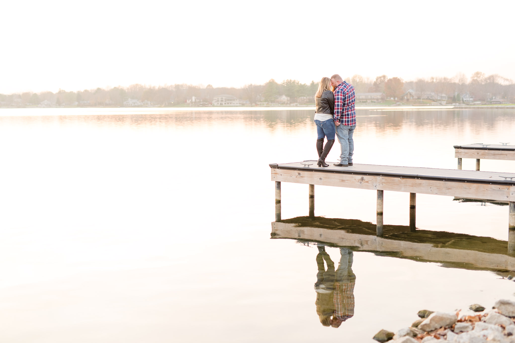 Engaged couple cuddle at the end of a pier.