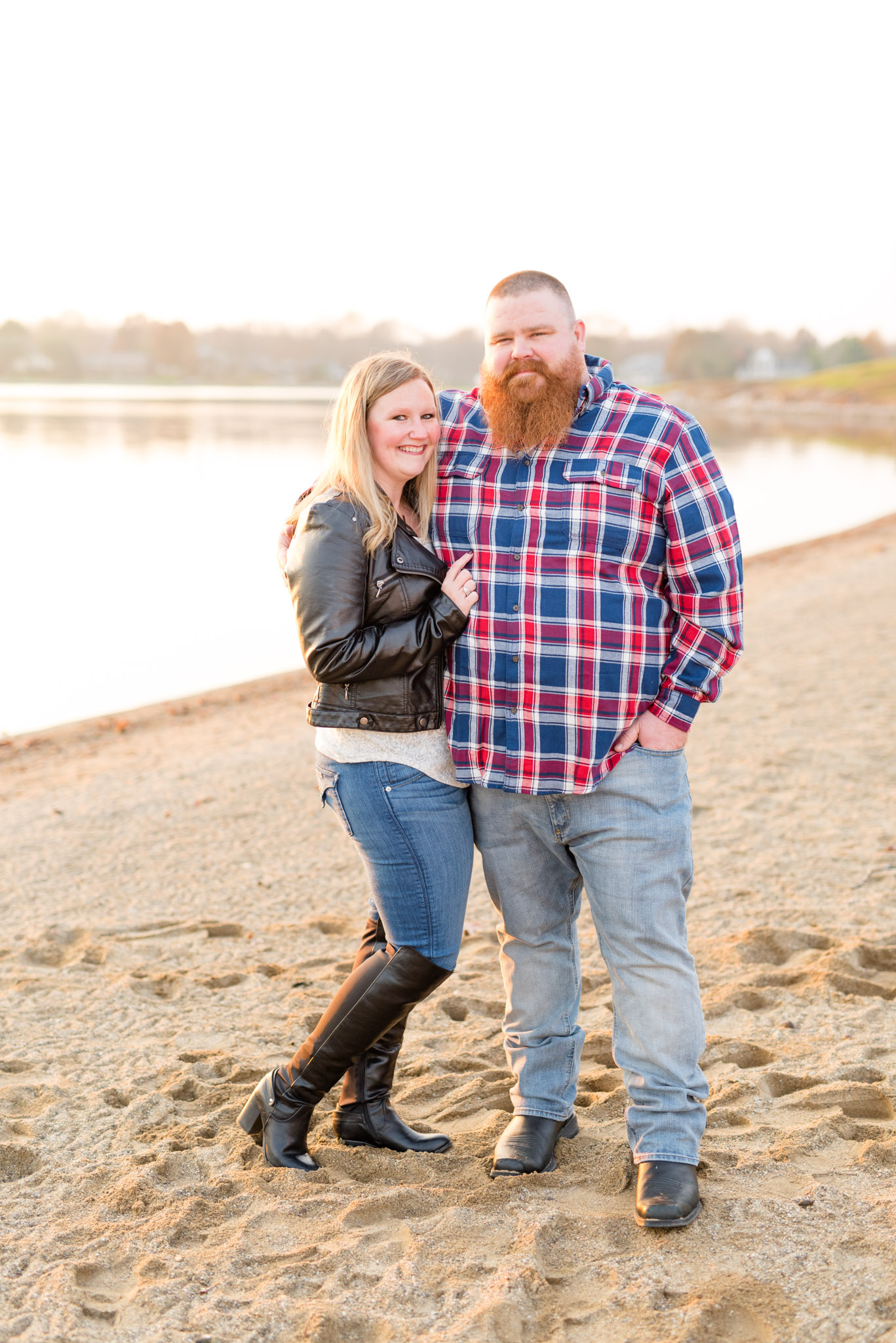 Engaged couple stand on beach and smile.