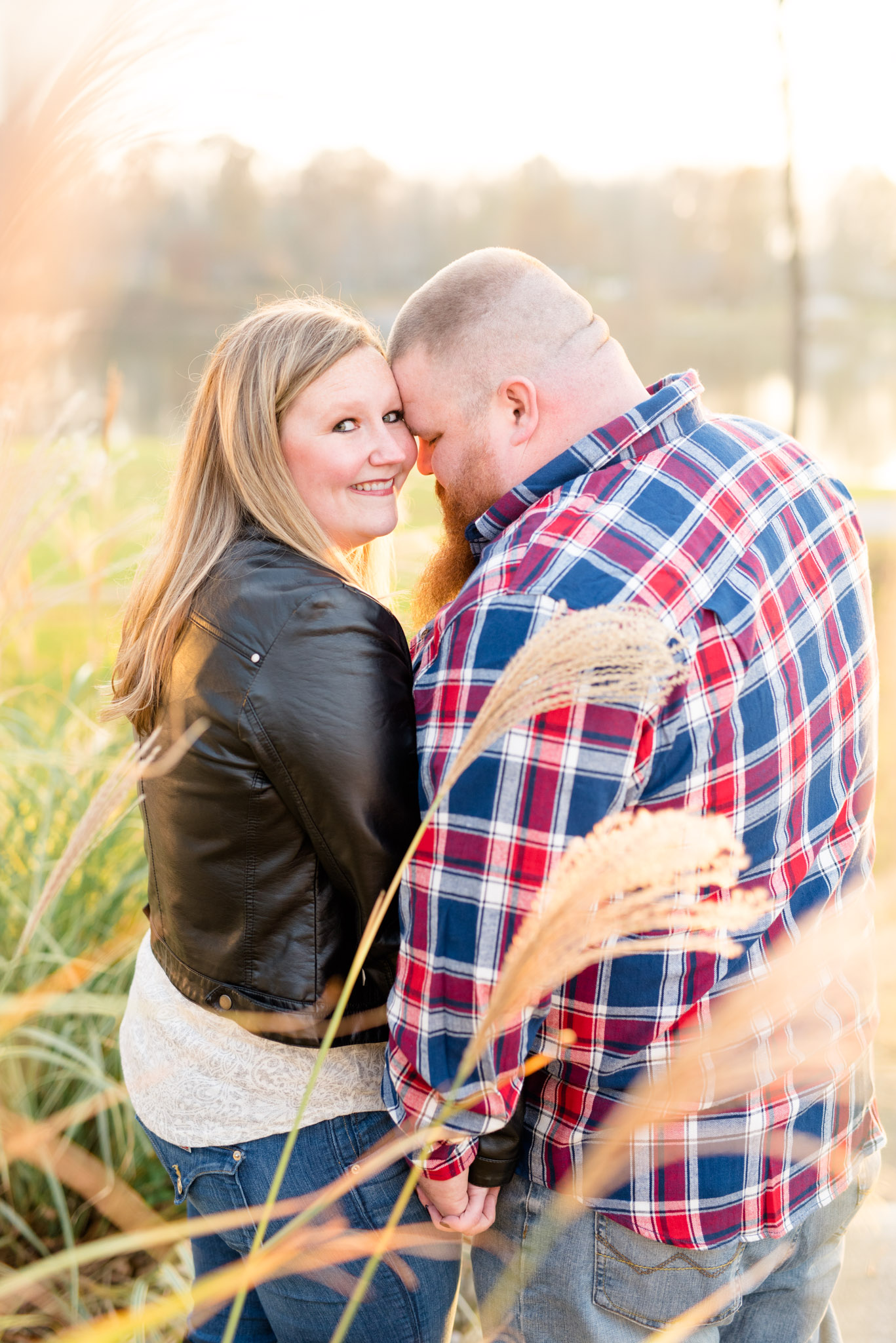 Engaged couple stands in field of tall grass at sunset.