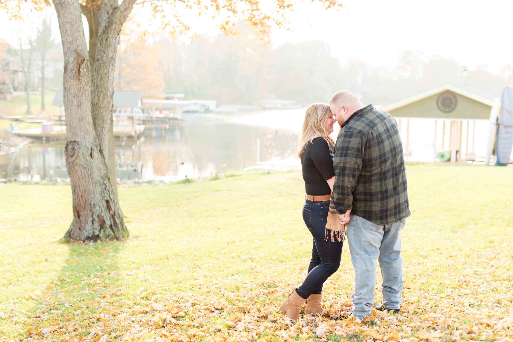 Engaged couple snuggle under tree.