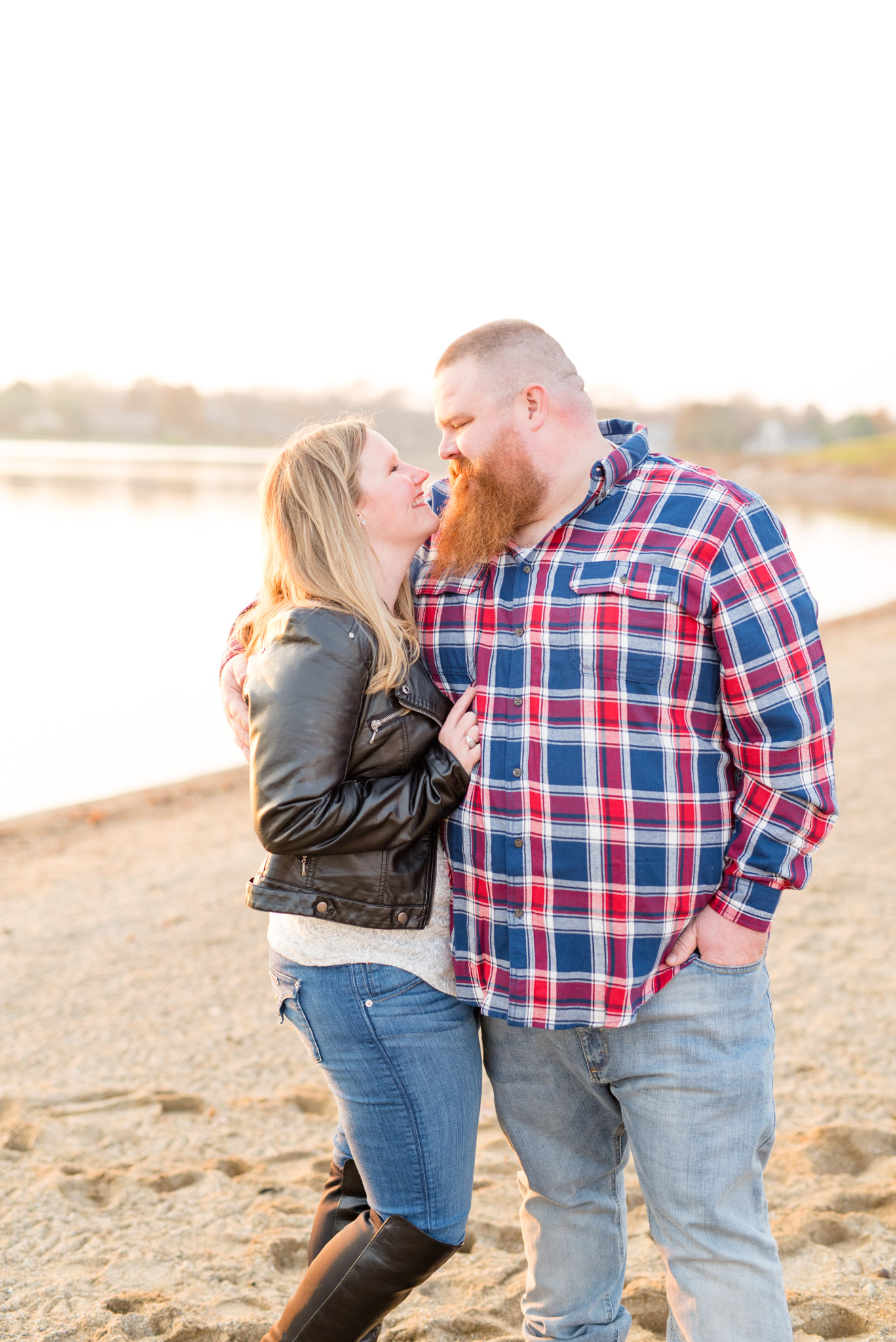 Engaged bride and groom smile at each other on beach.