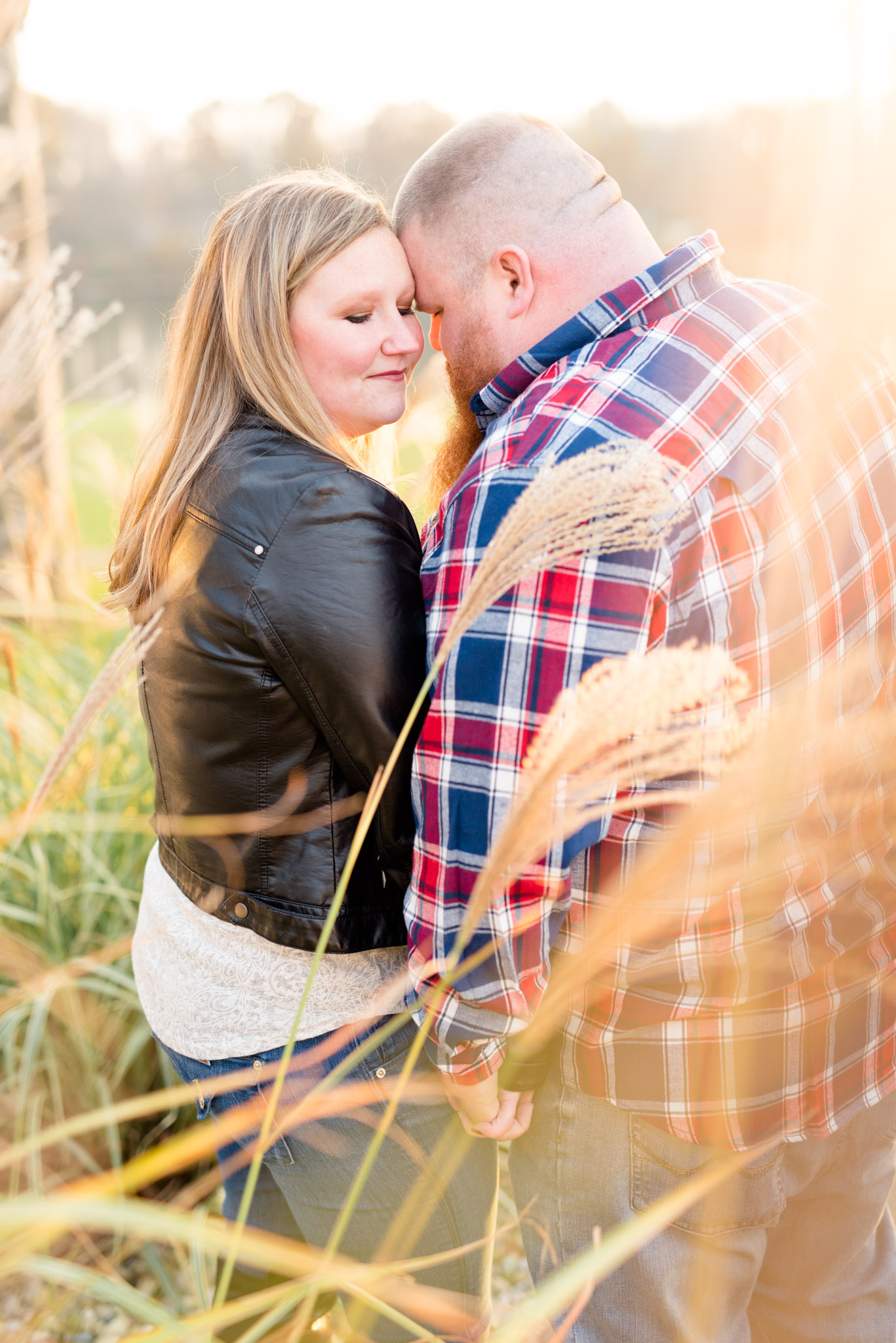 Engaged couple cuddles in field of tall grass.