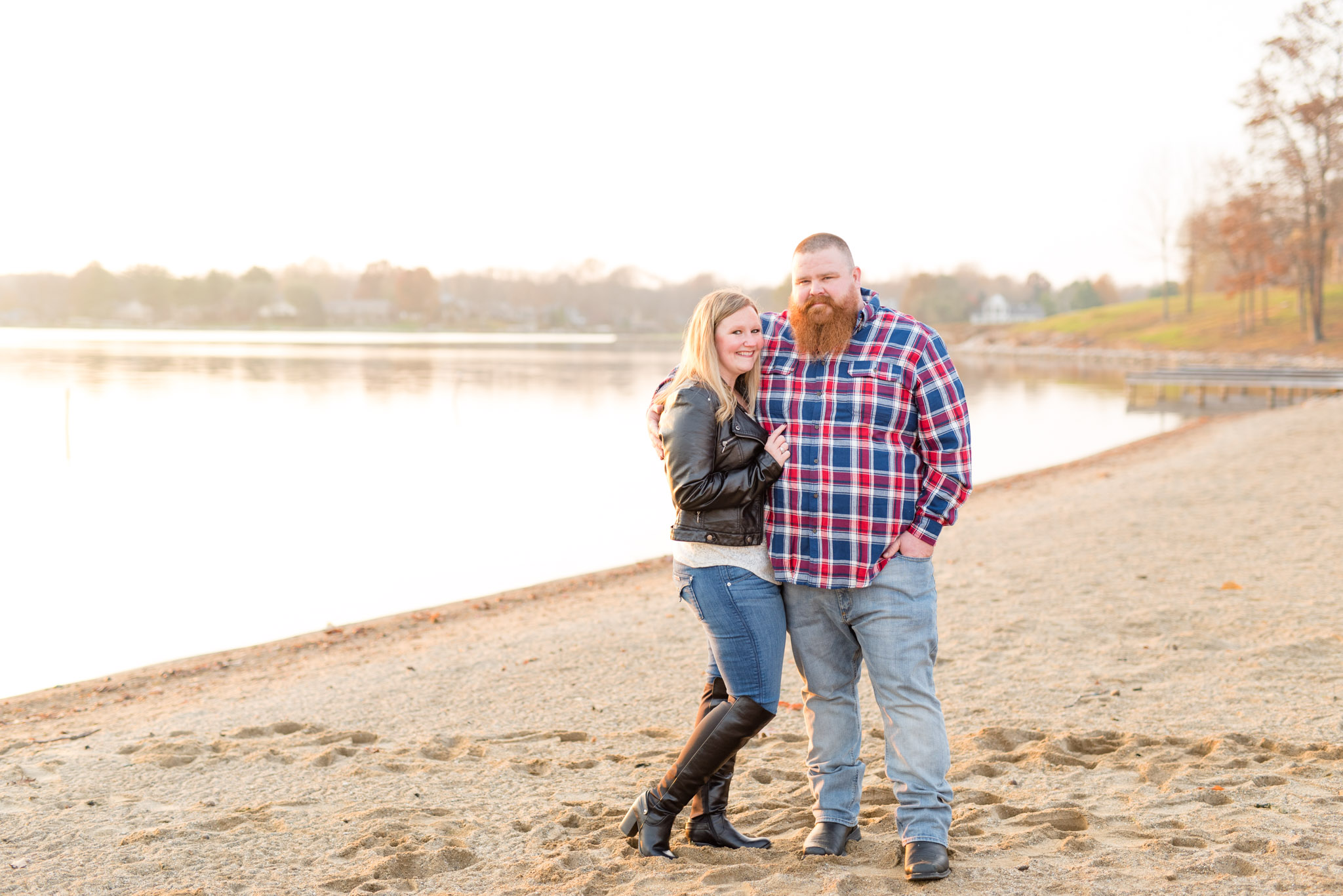 Engaged couple stand on beach at sunset.