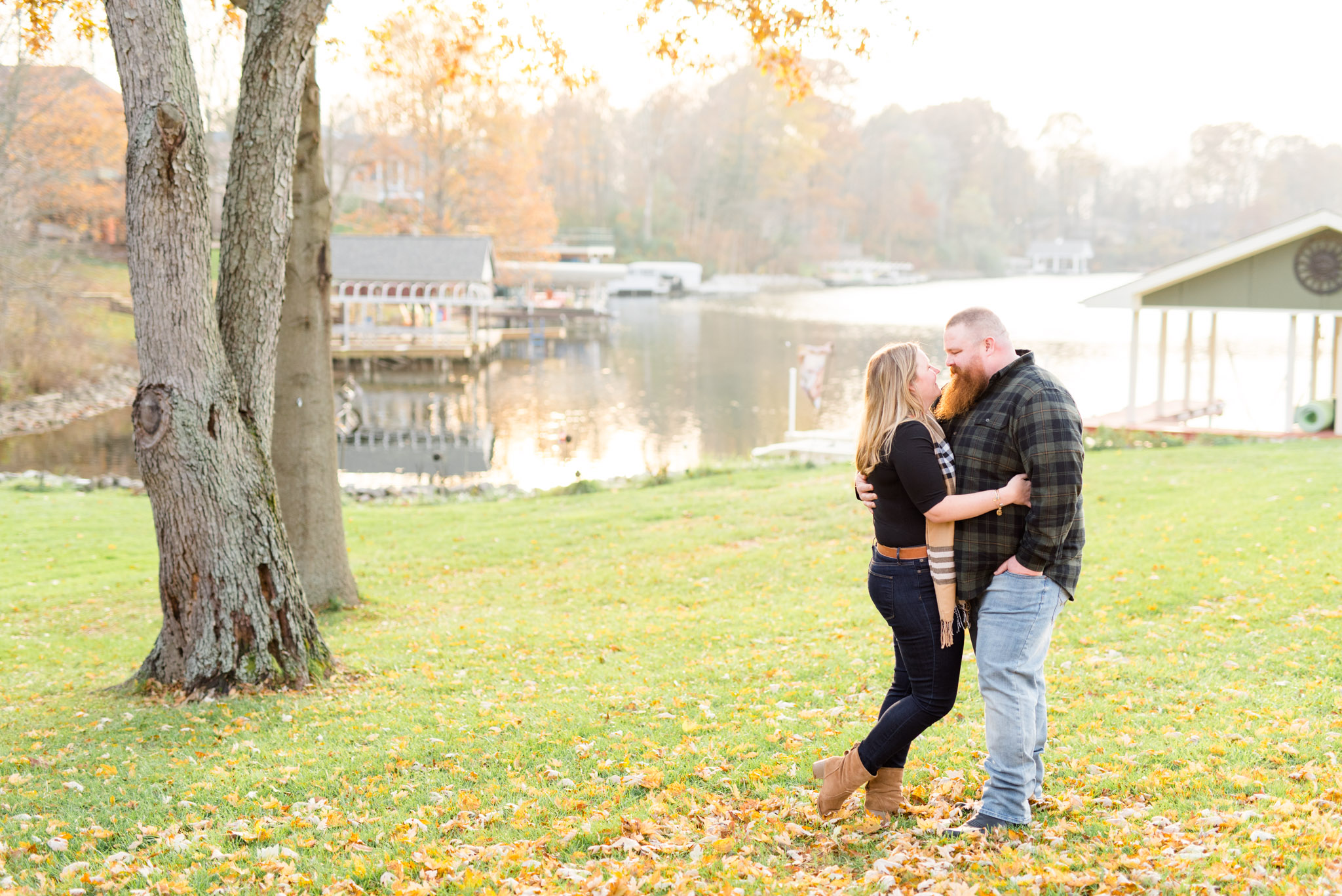 Bride and groom smile at each other under fall tree.