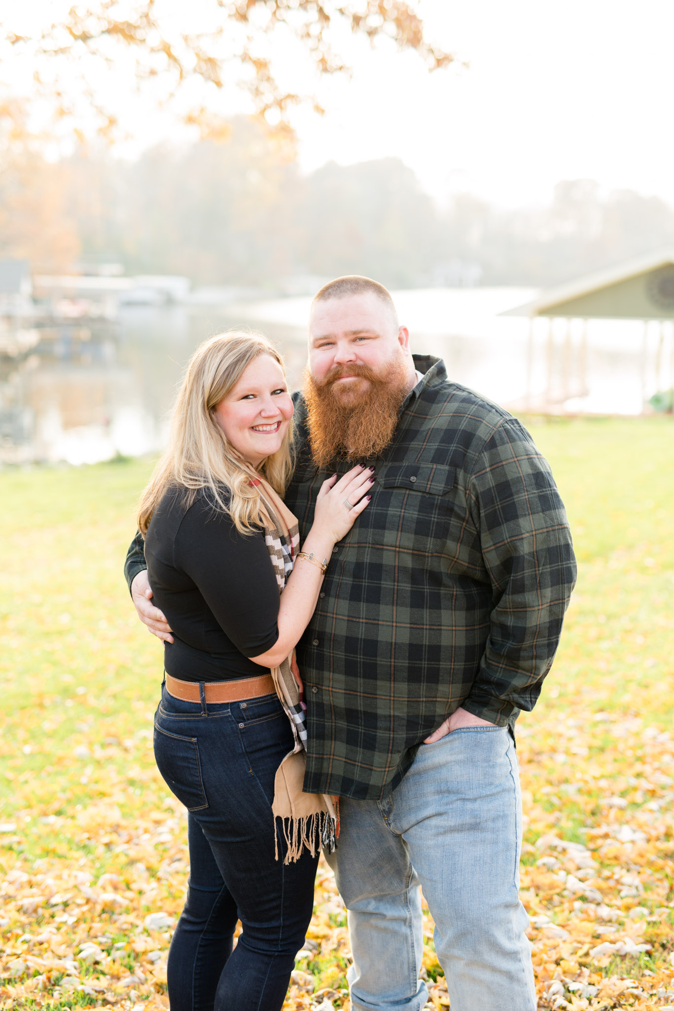 Engaged couple smiles at camera during fall.