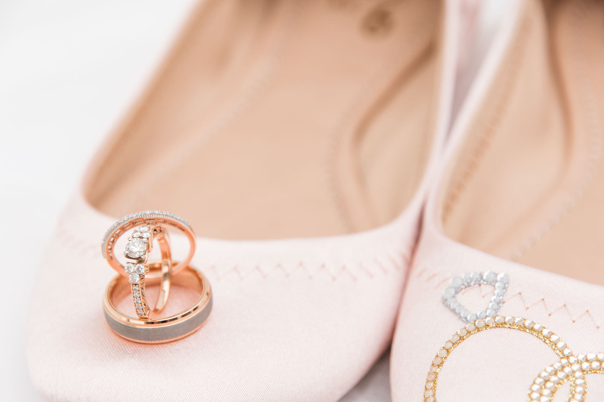Rose gold engagement ring and wedding bands sit on brides shoes.