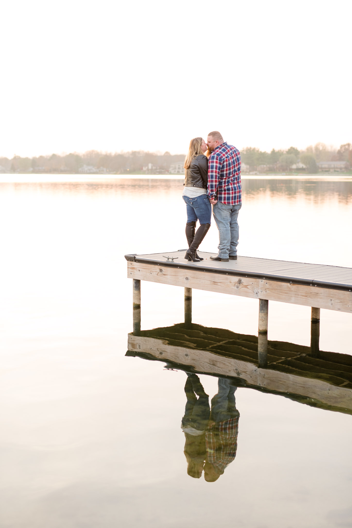Engaged couple stand on dock at sunset.