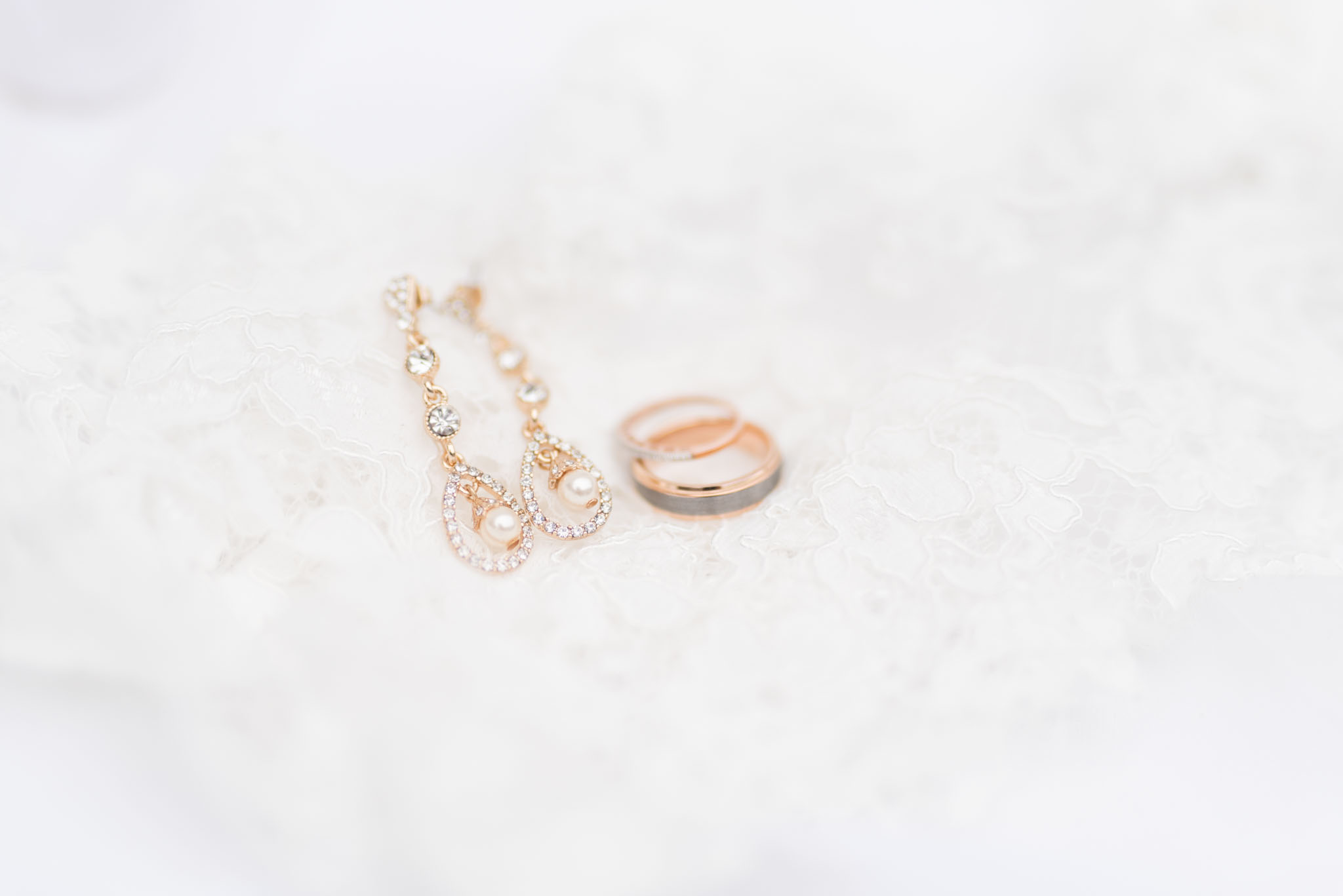 Bridal earrings and wedding bands sit on lace.