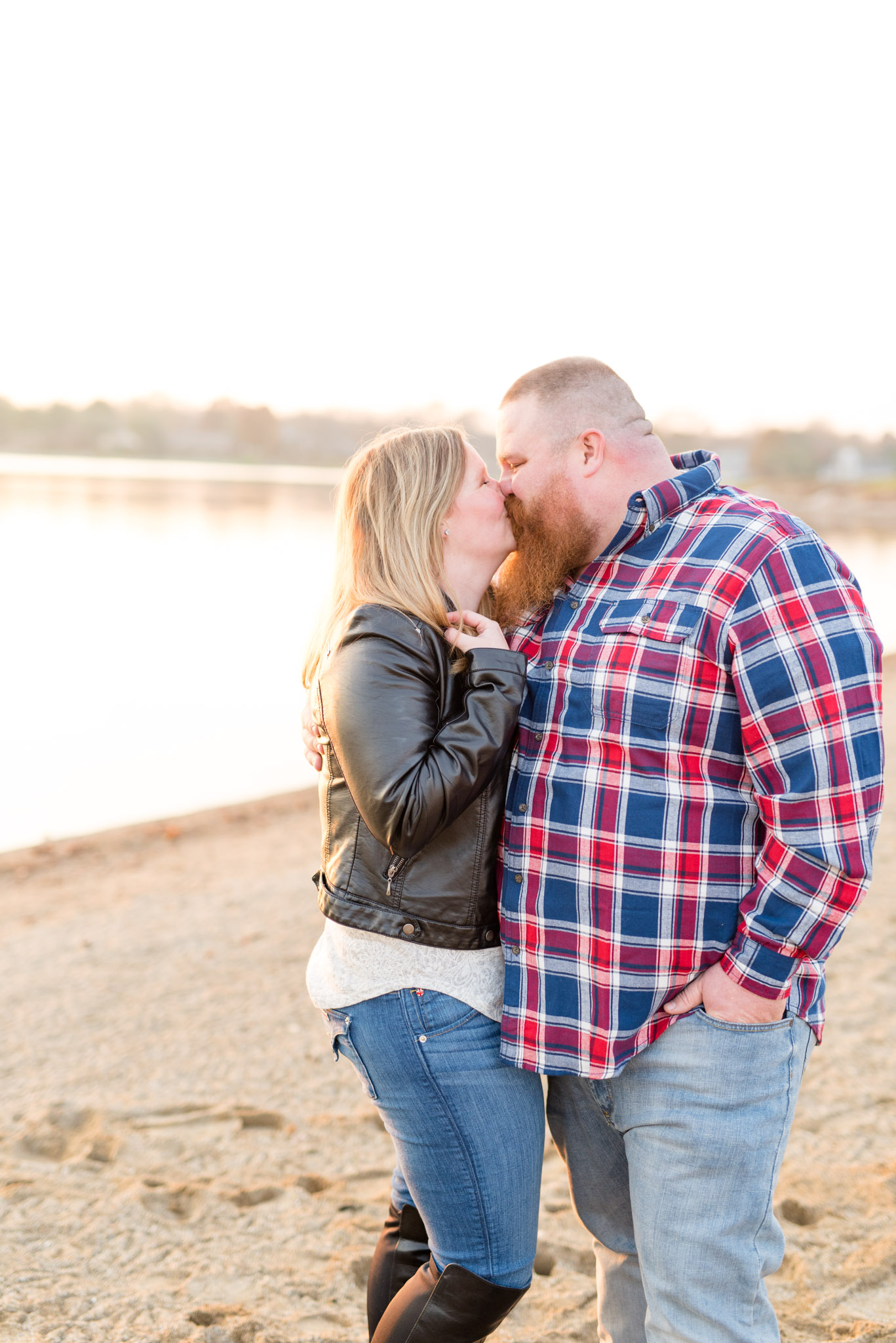 Engaged couple kisses at sunset on beach.