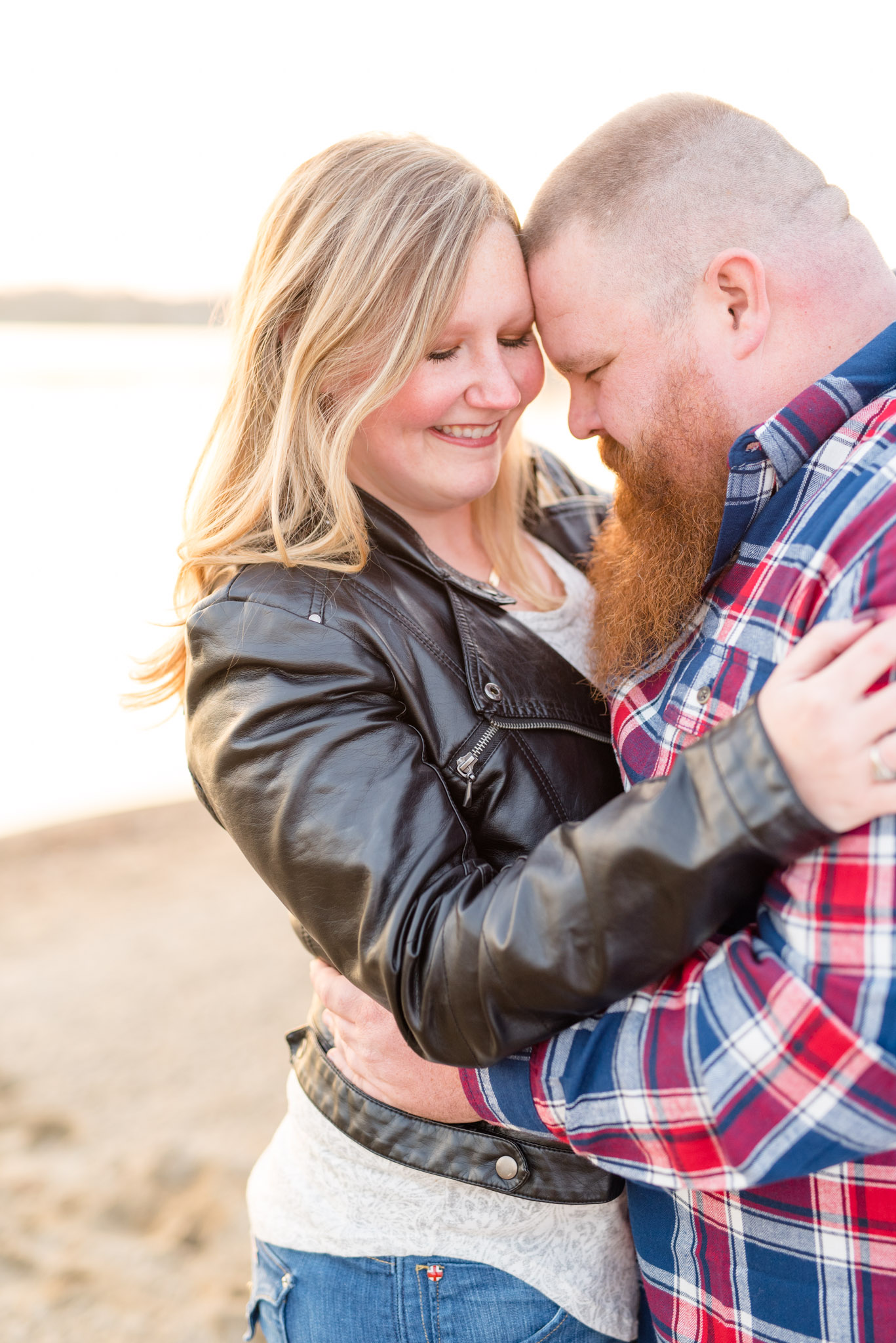 Engaged bride and groom smile and hug on a sunset beach.