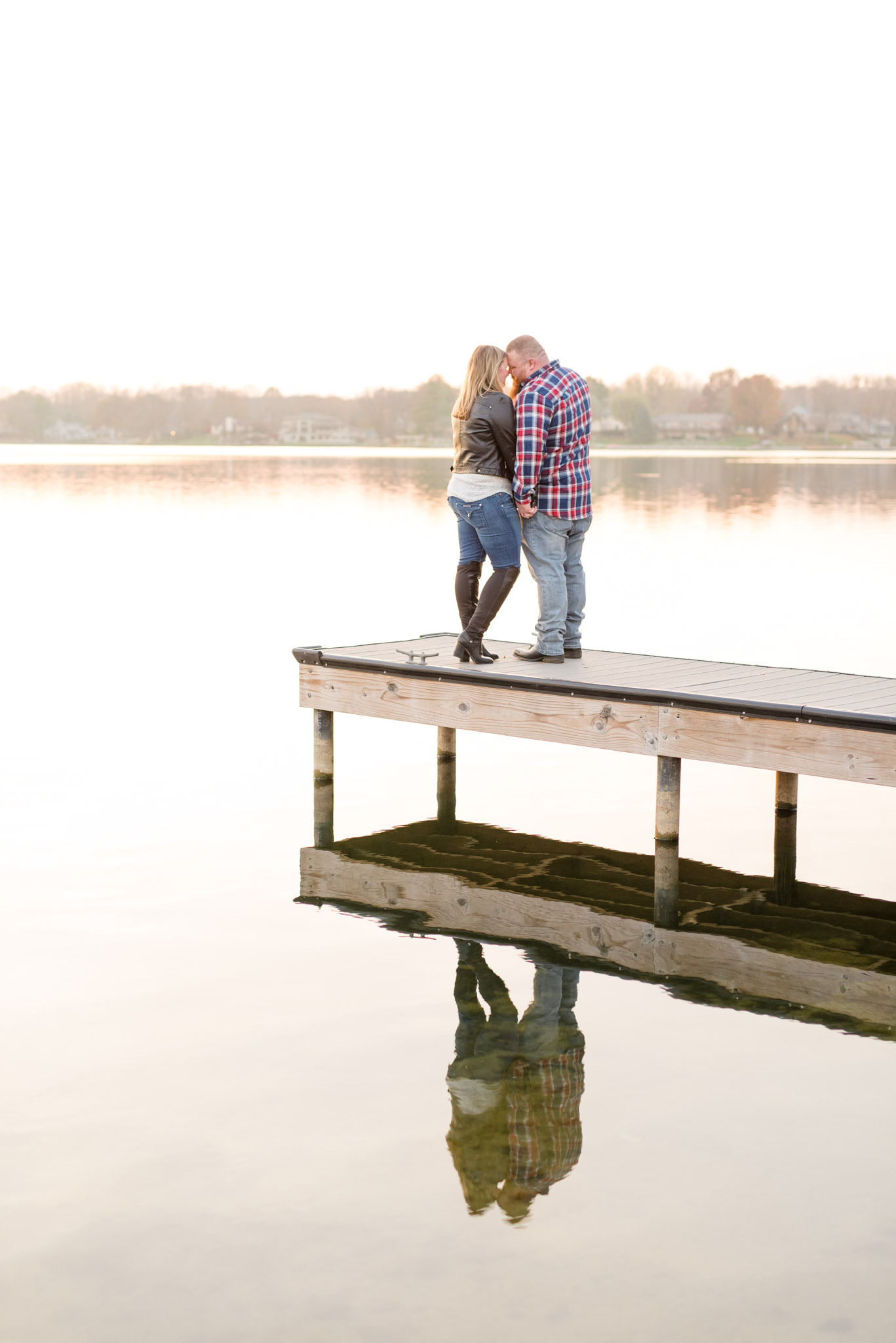 Engaged couple stand on a pier and smile.