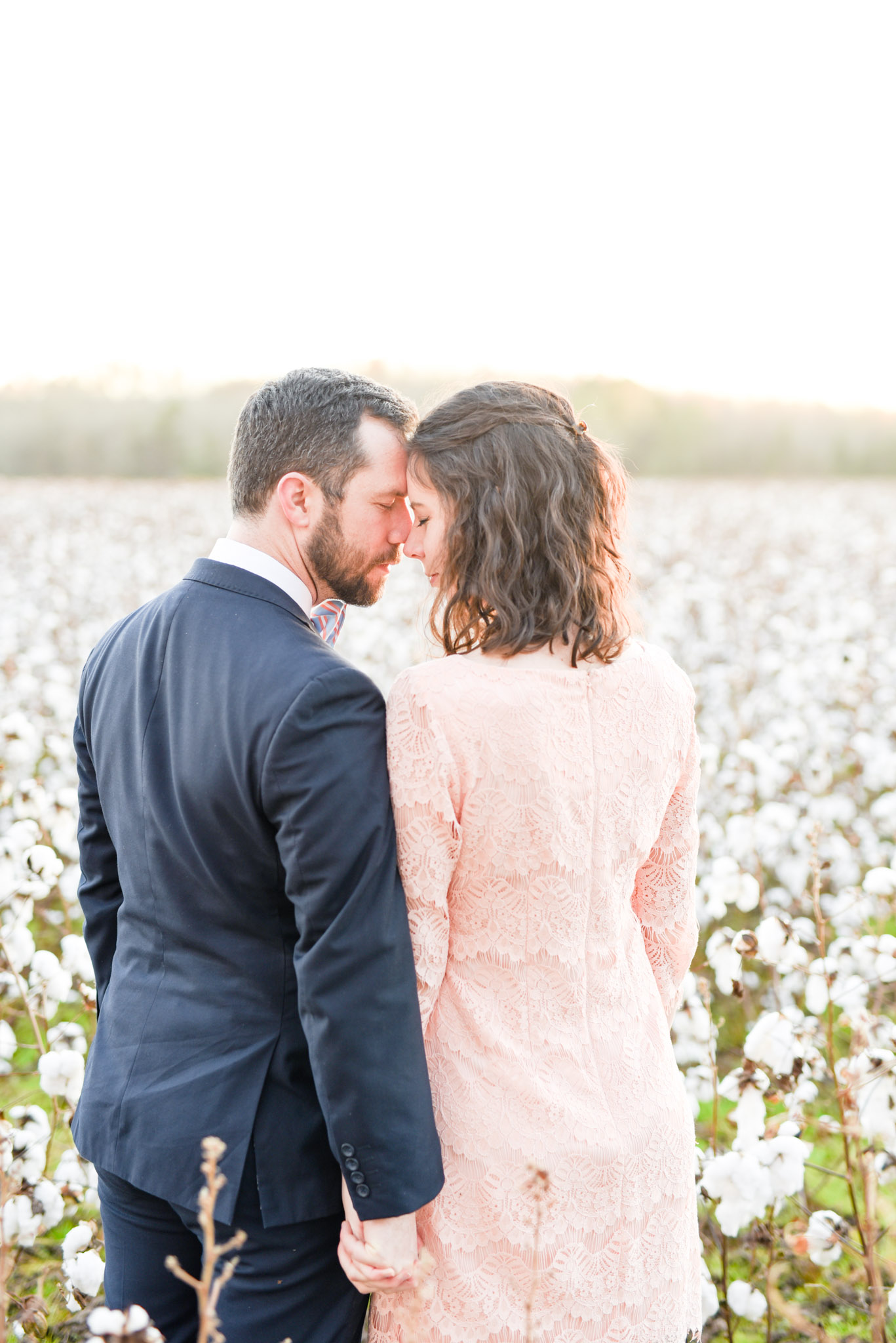 Man and woman snuggle in cotton field at sunset.