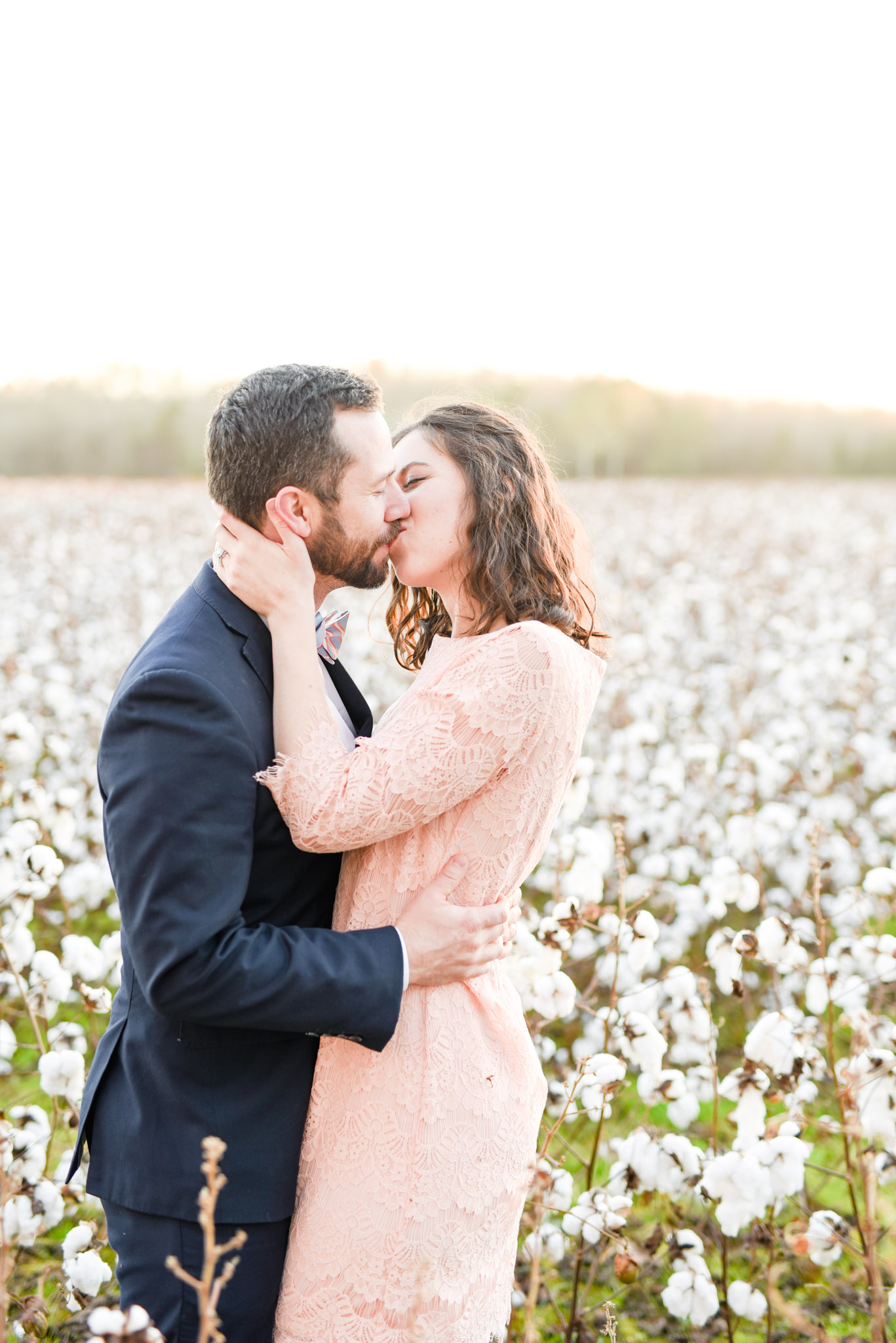 Couple kisses at sunset in cotton field.