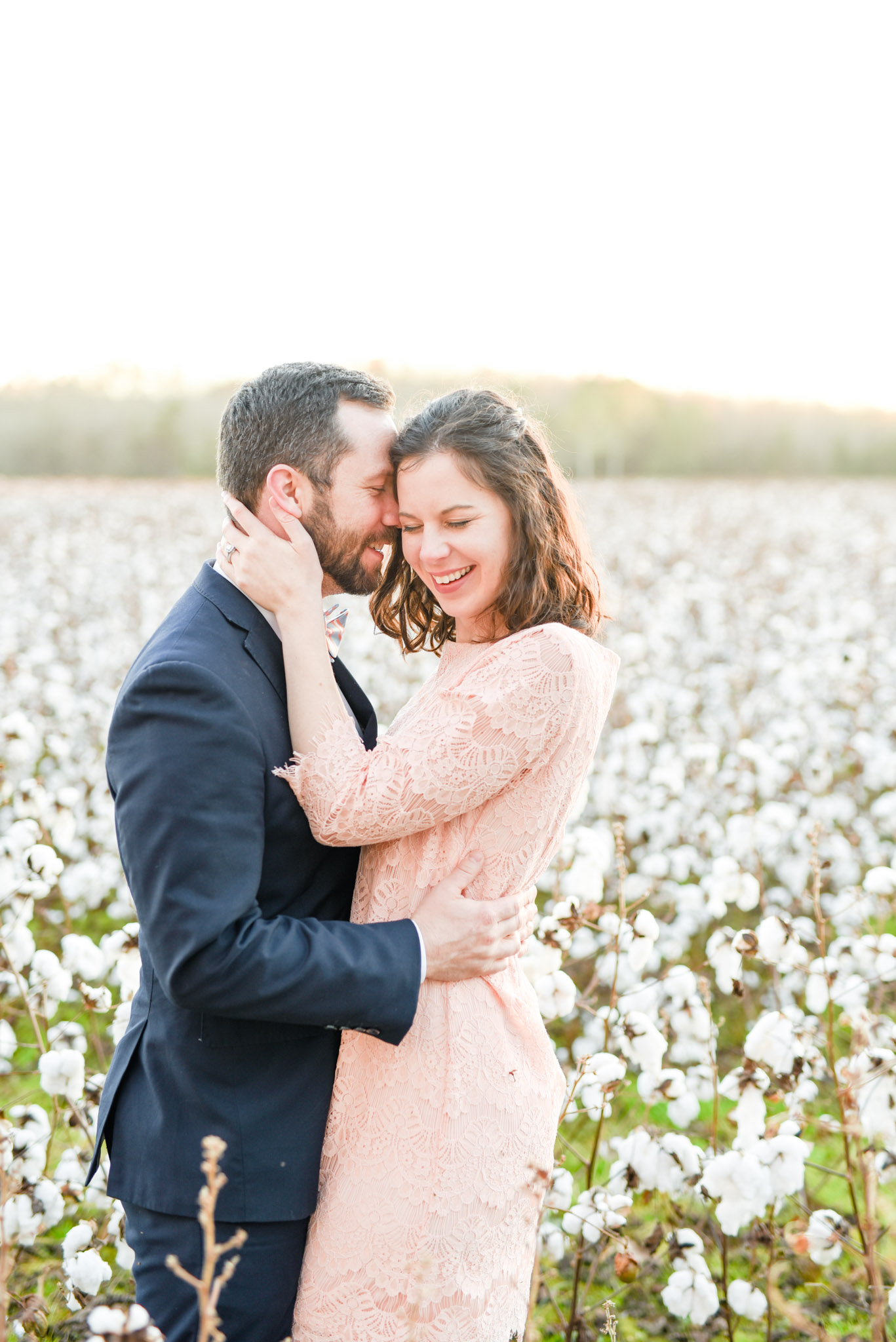 Man and woman laugh at sunset in cotton field.