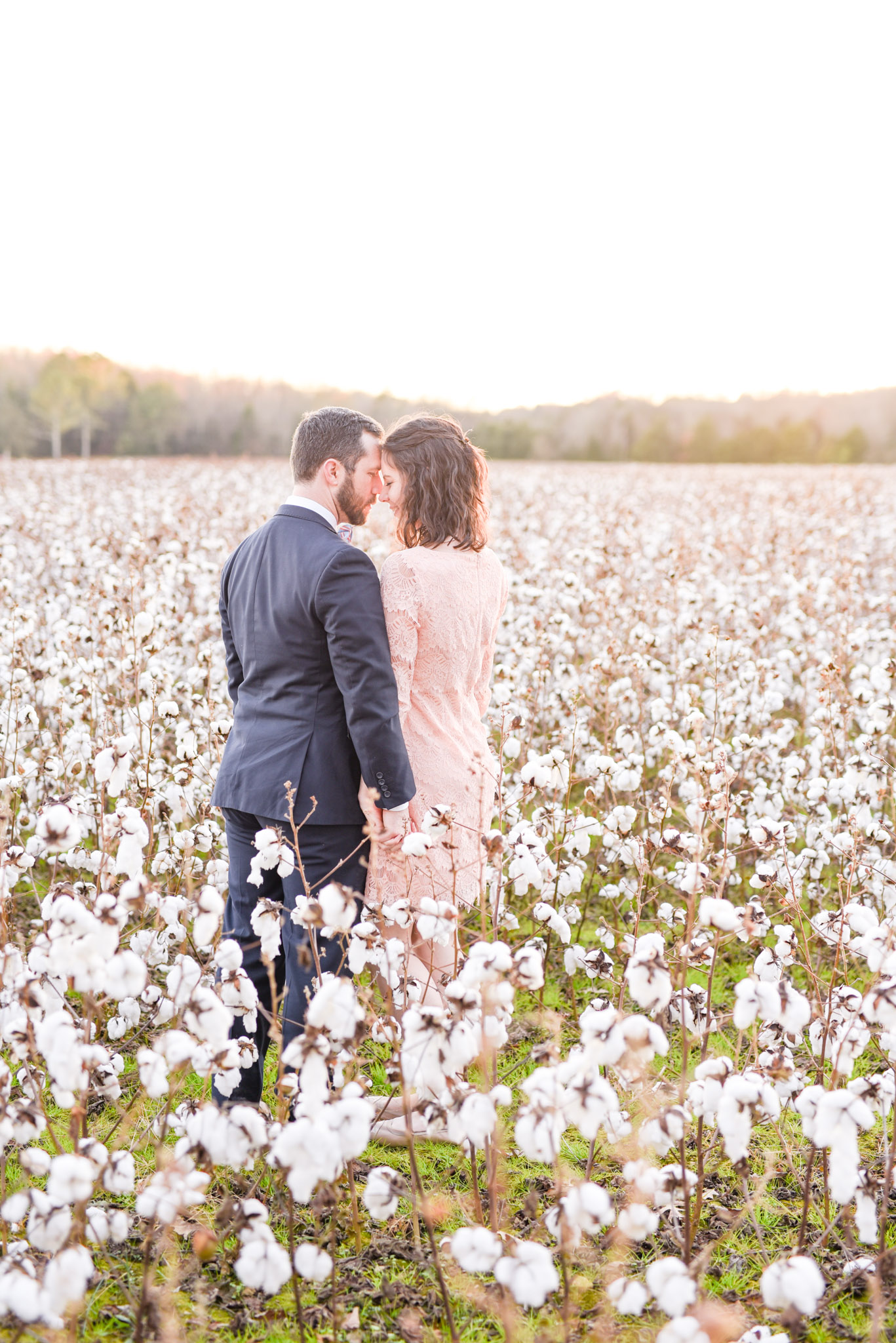 Couple leans heads together in cotton field.