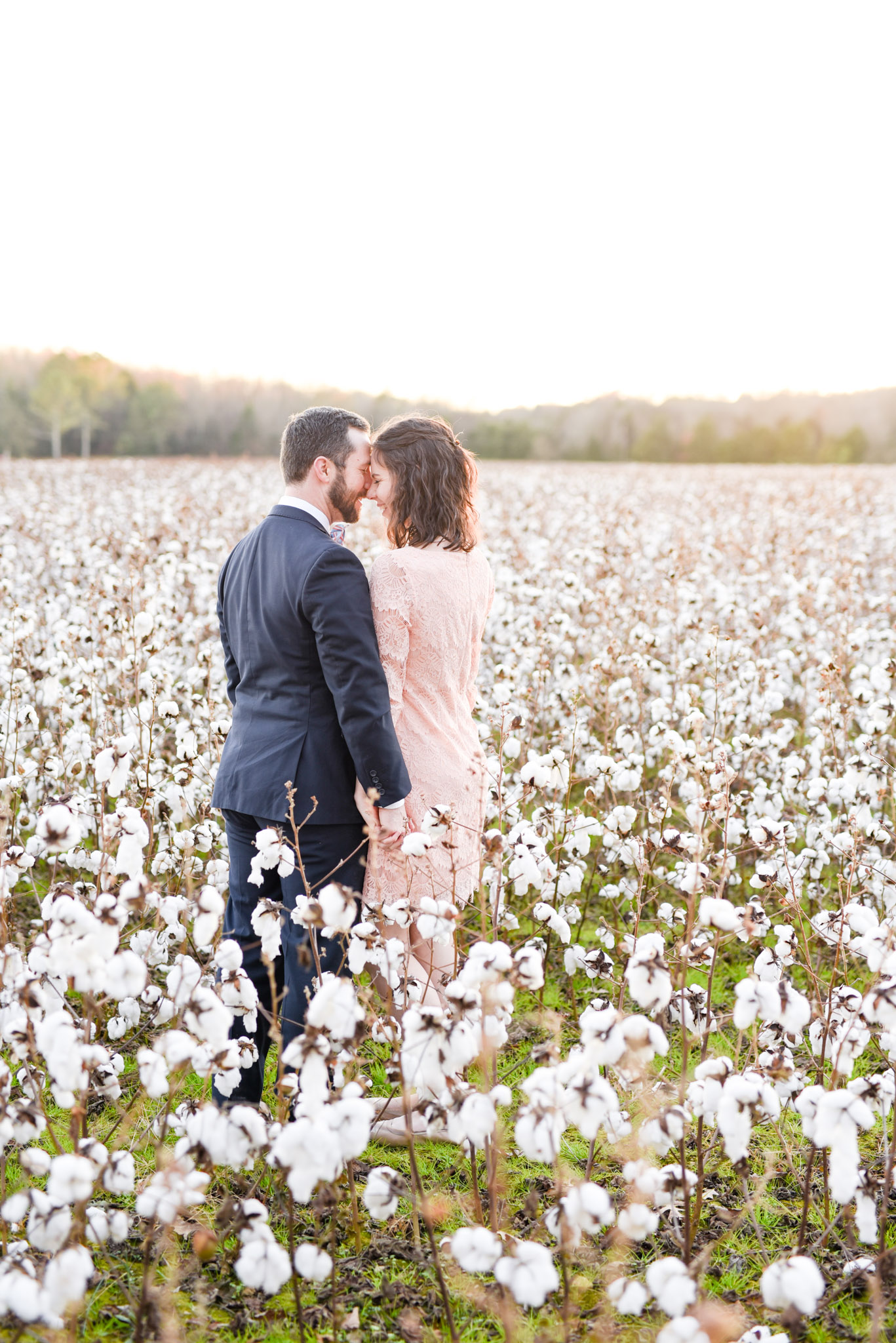Couple leans on each other in cotton field.