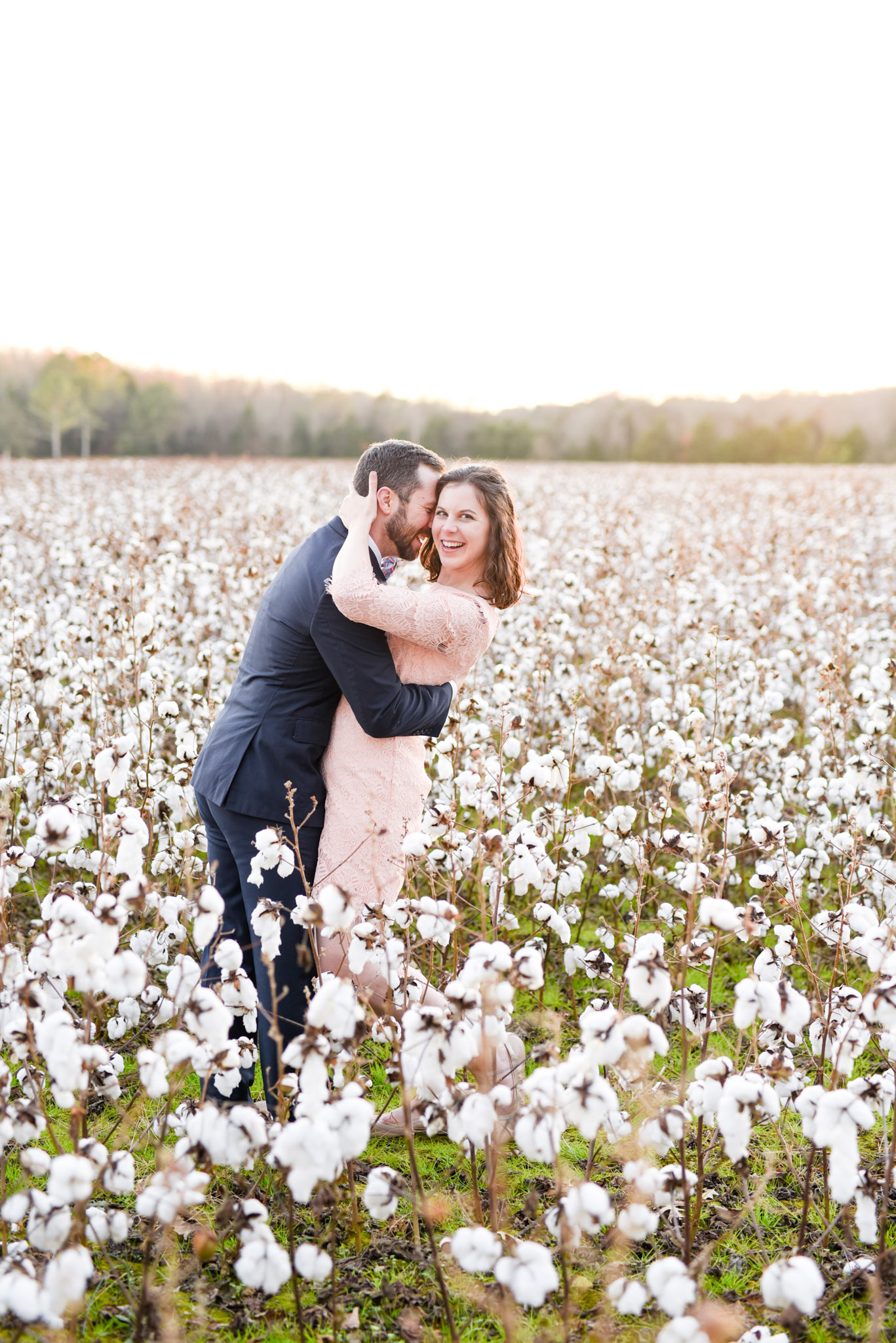 Couple laughs standing in cotton field.