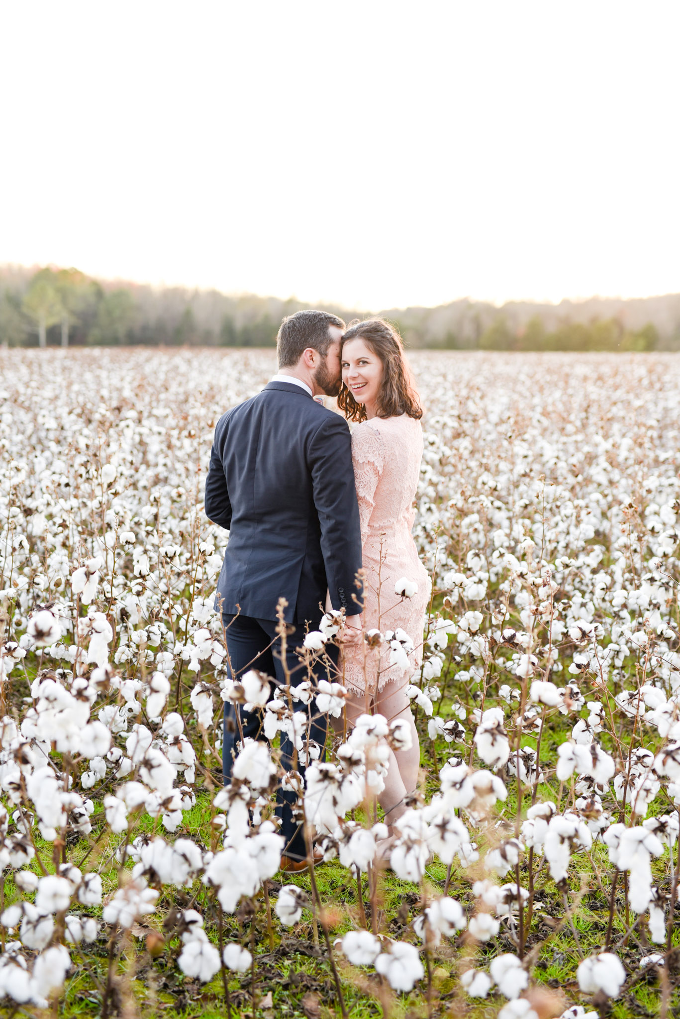 Woman smiles while holding hands with husband in cotton field.