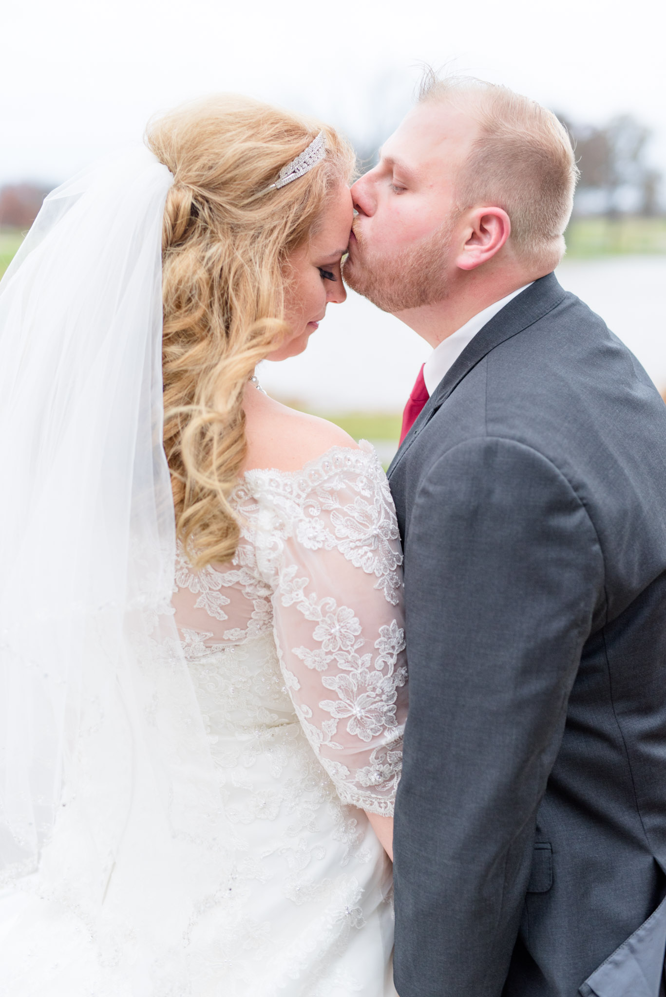 Groom kisses bride on forehead during wedding portraits.
