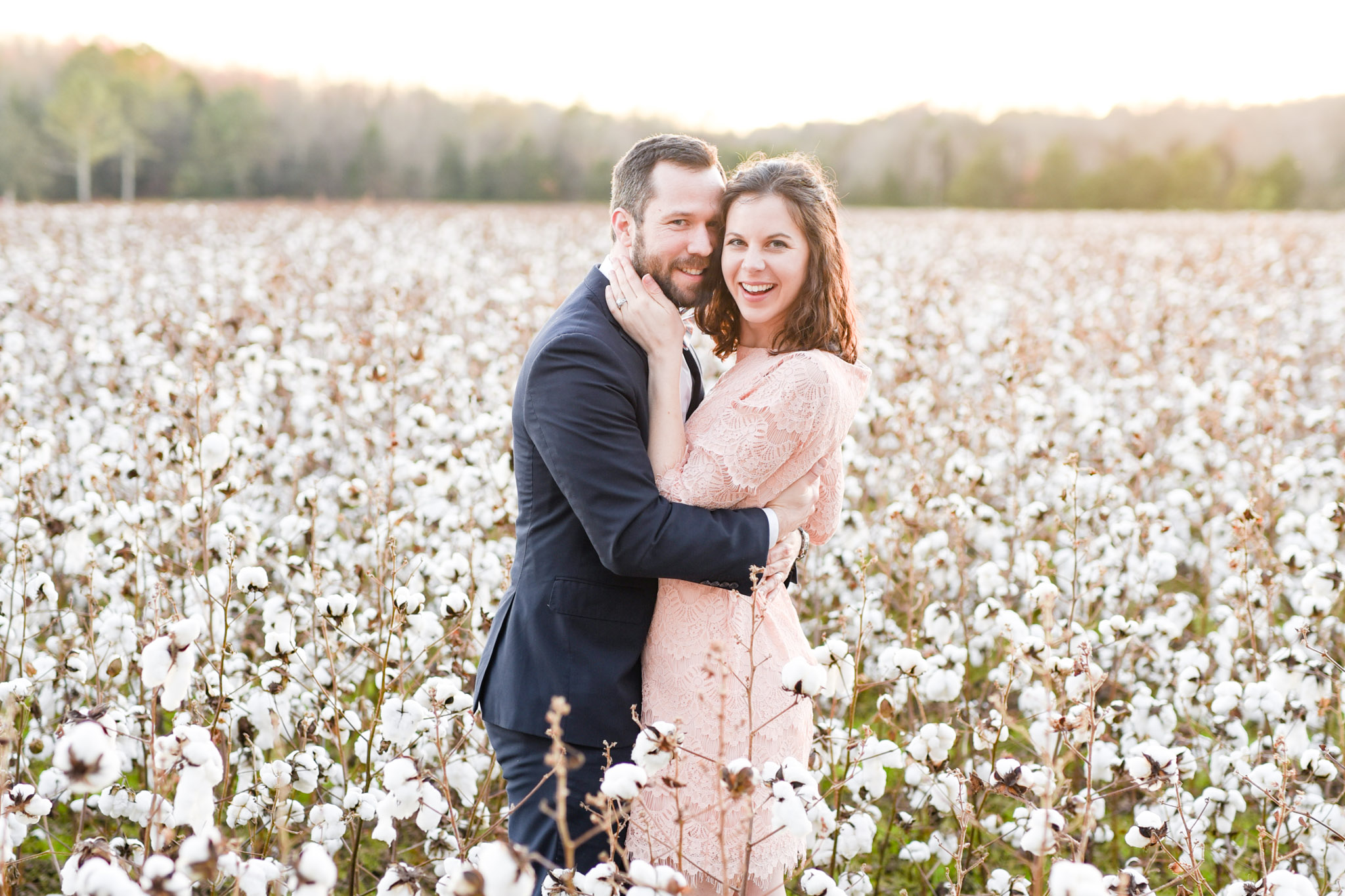 Couples stands in cotton field at sunset.