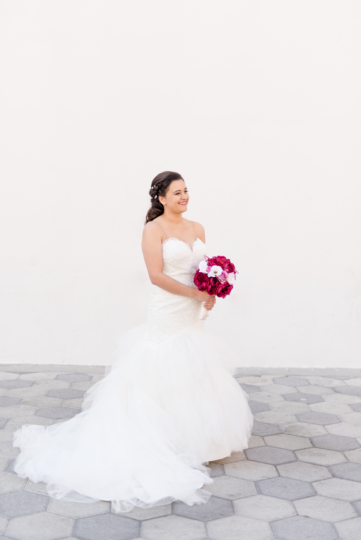 Bride smiles off camera in front of white wall.