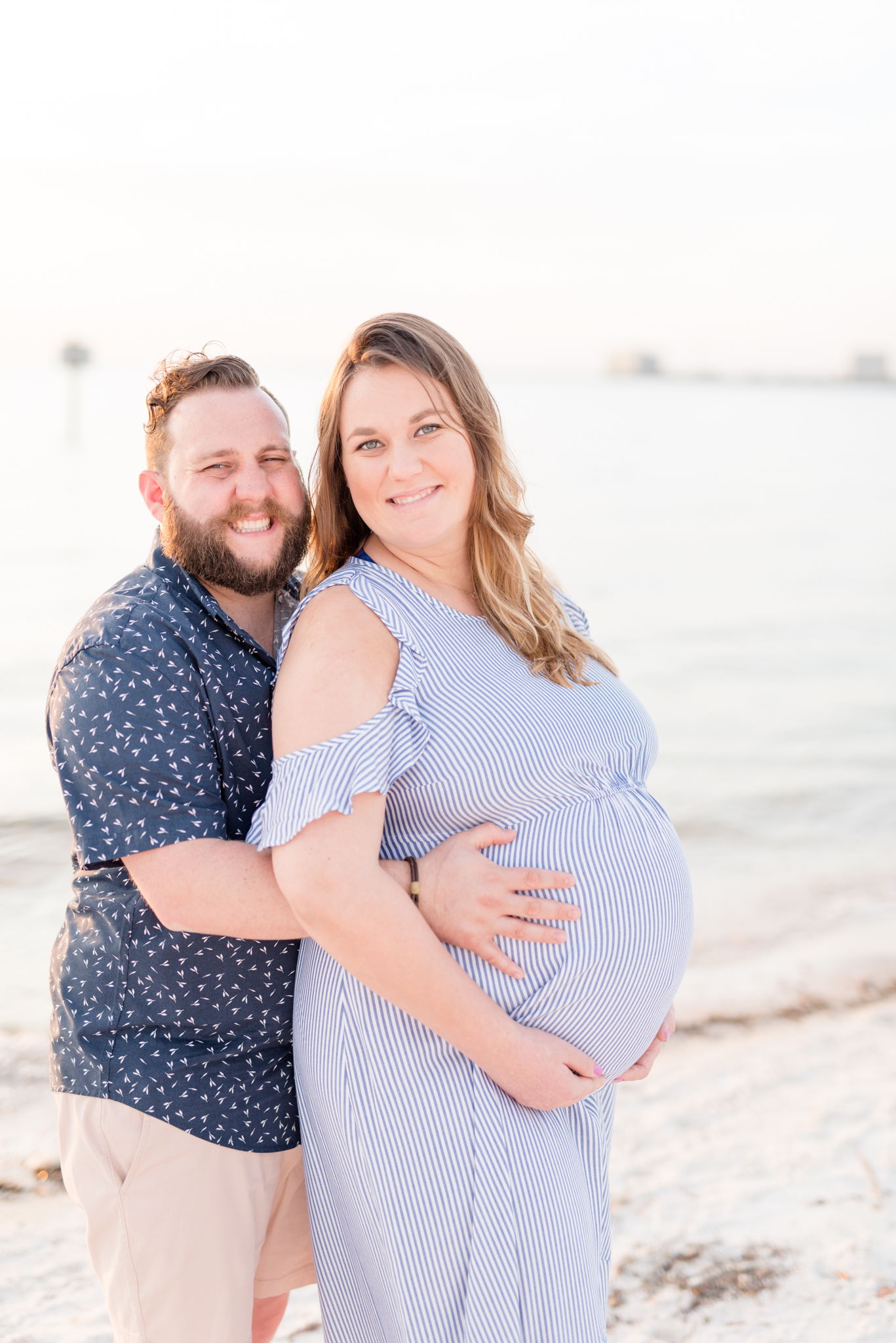 Expecting Couple Looks at Camera on Beach