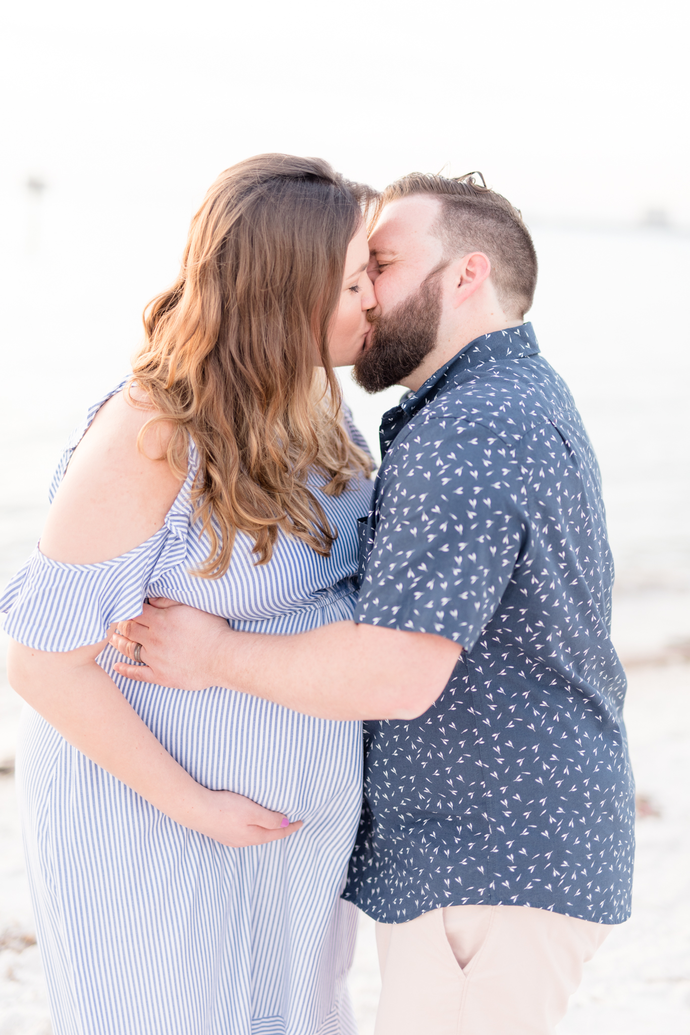 Couple expecting twins kisses on beach.