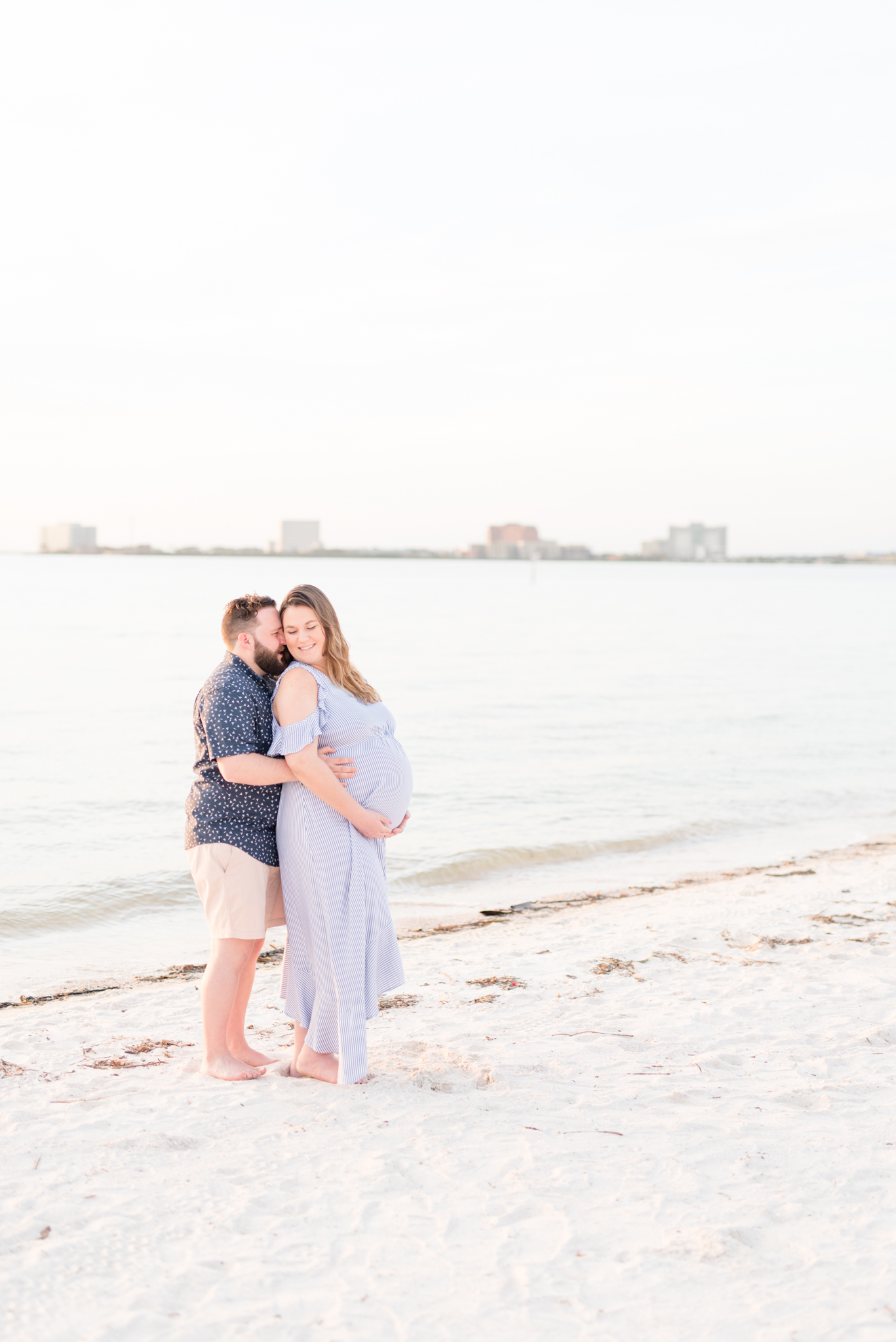 Couple expecting twins stands on beach.