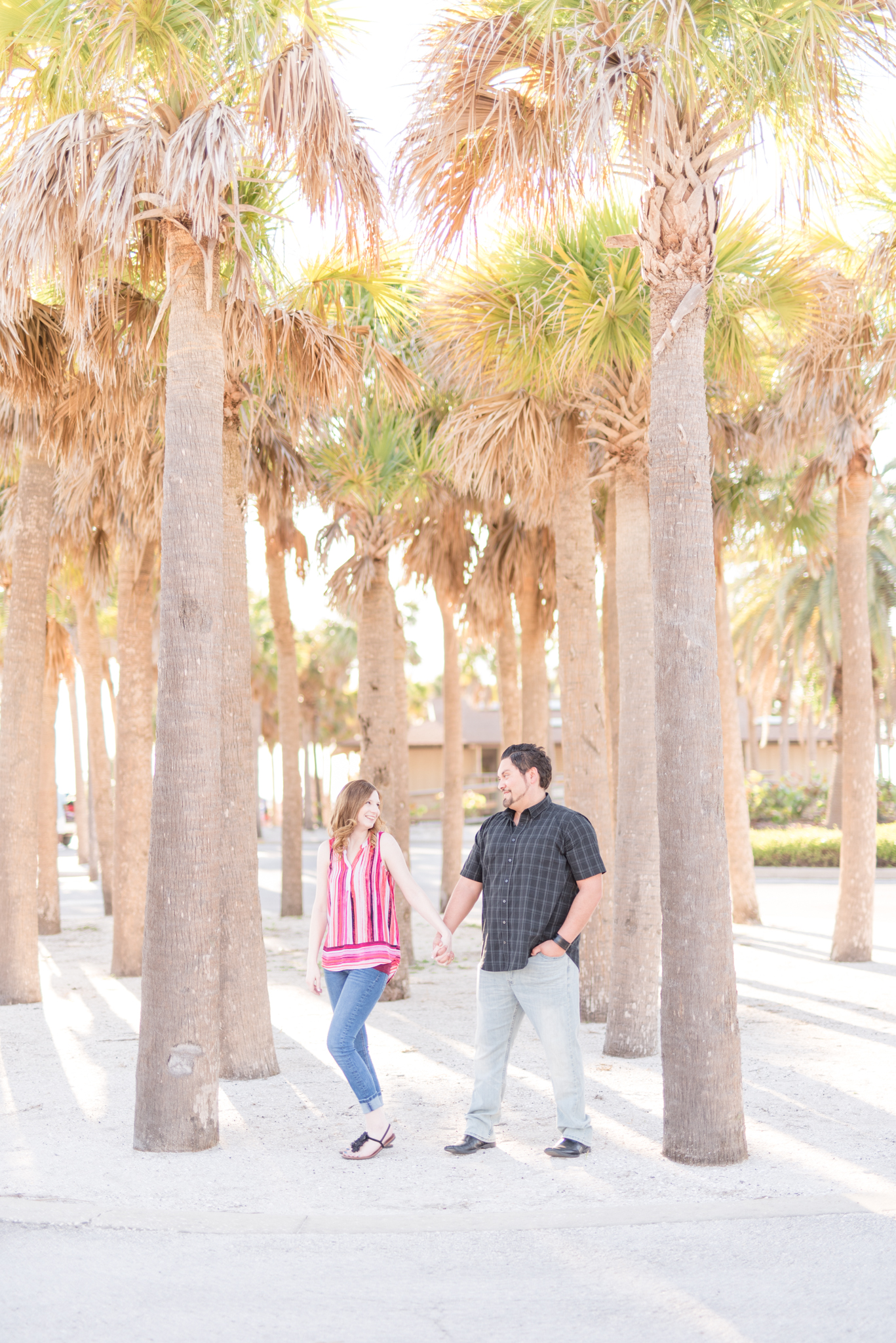 Couple stands near palm trees.