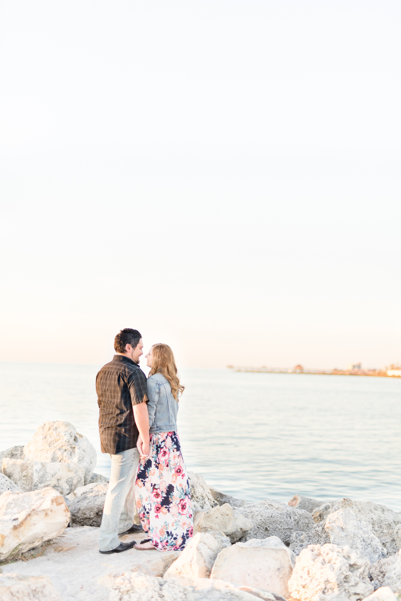 Couple stands on rocks next to ocean.