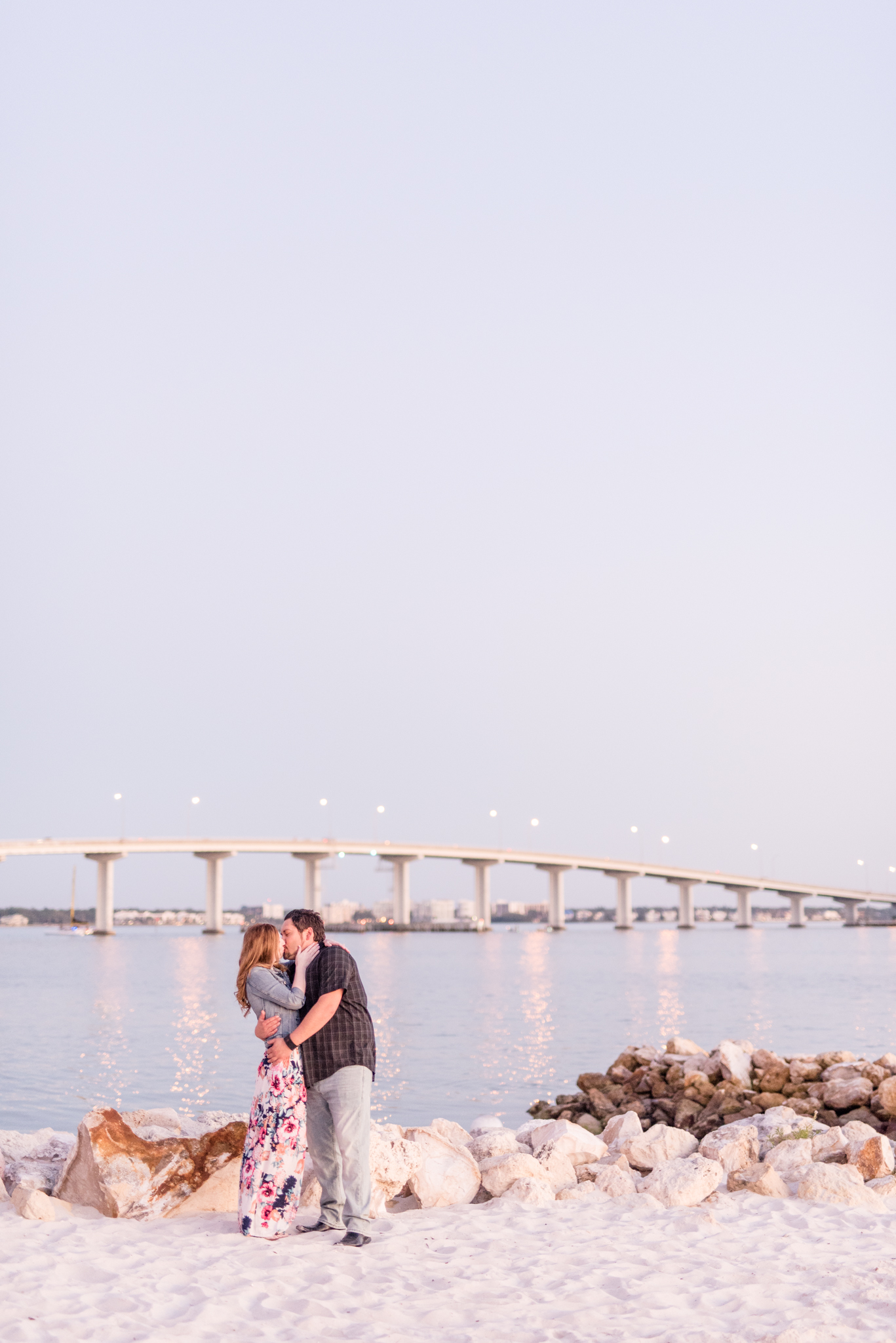 Couple kisses in front of large bridge.