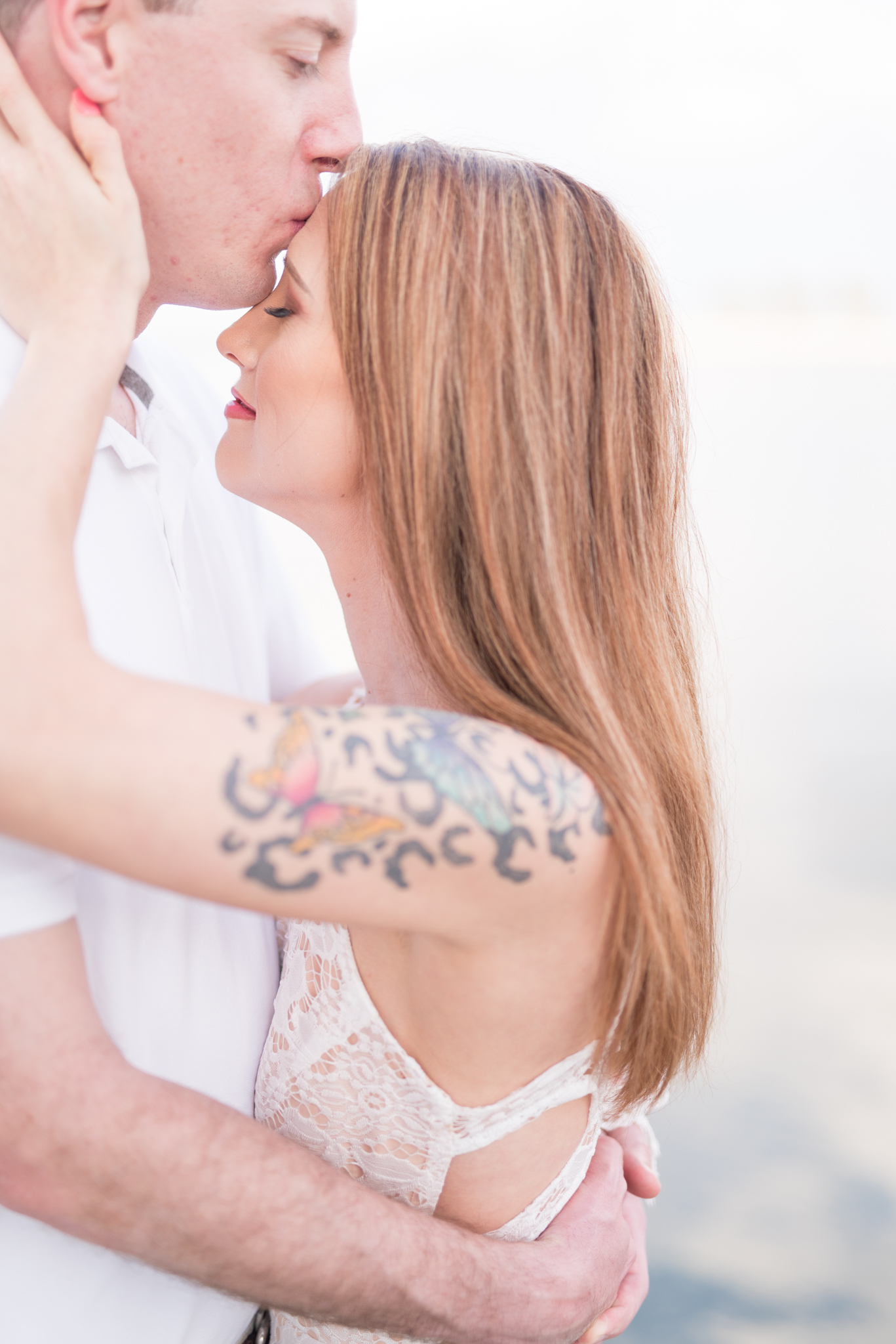 Man kisses woman on forehead by ocean.