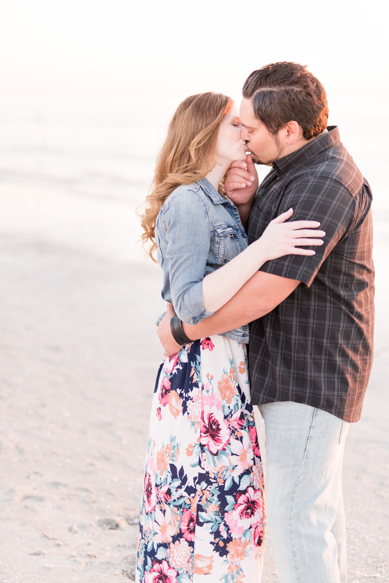 Engaged couple kisses on beach.