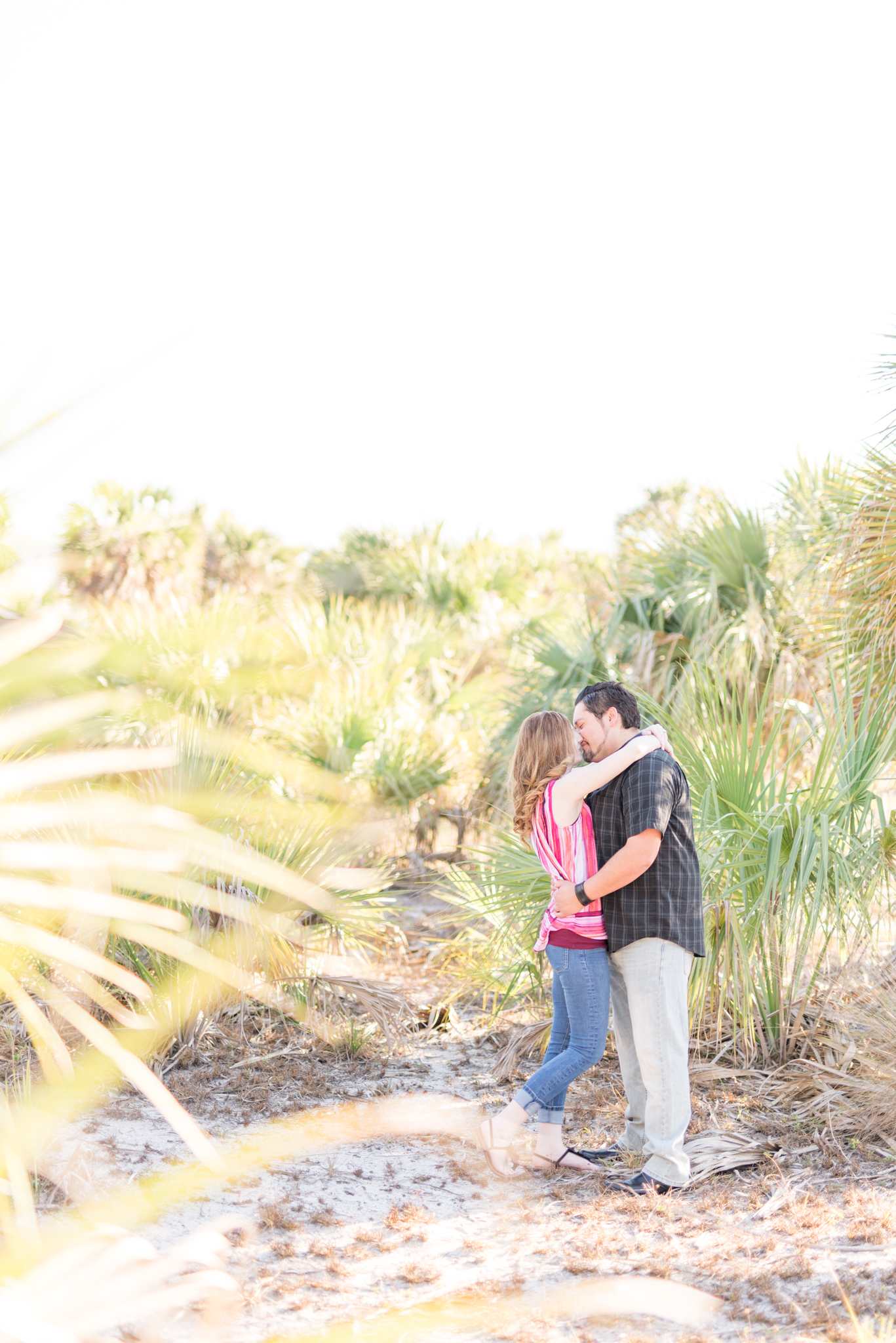 Engaged couple stands near small palm trees.