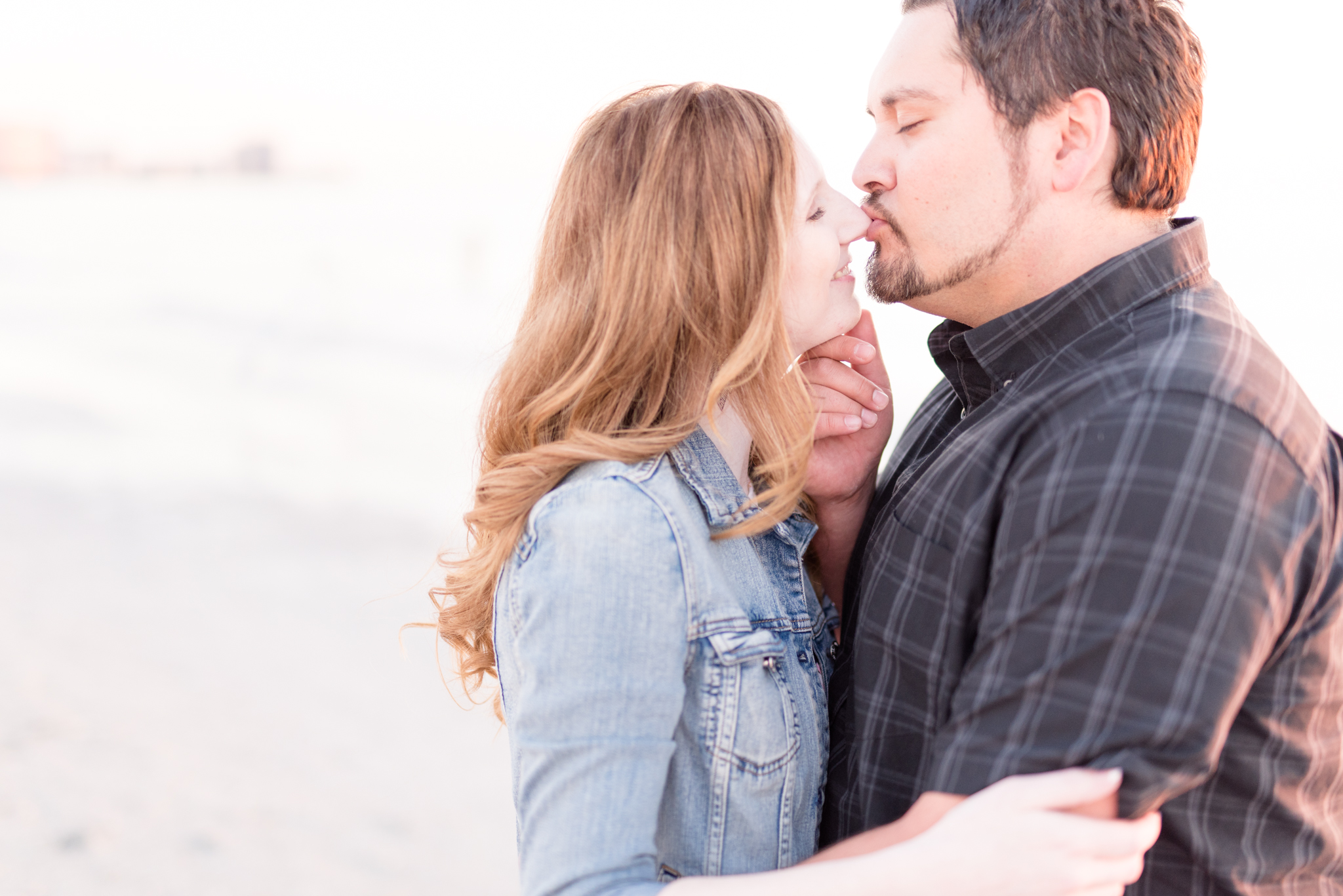 Man kisses fiances nose on beach.
