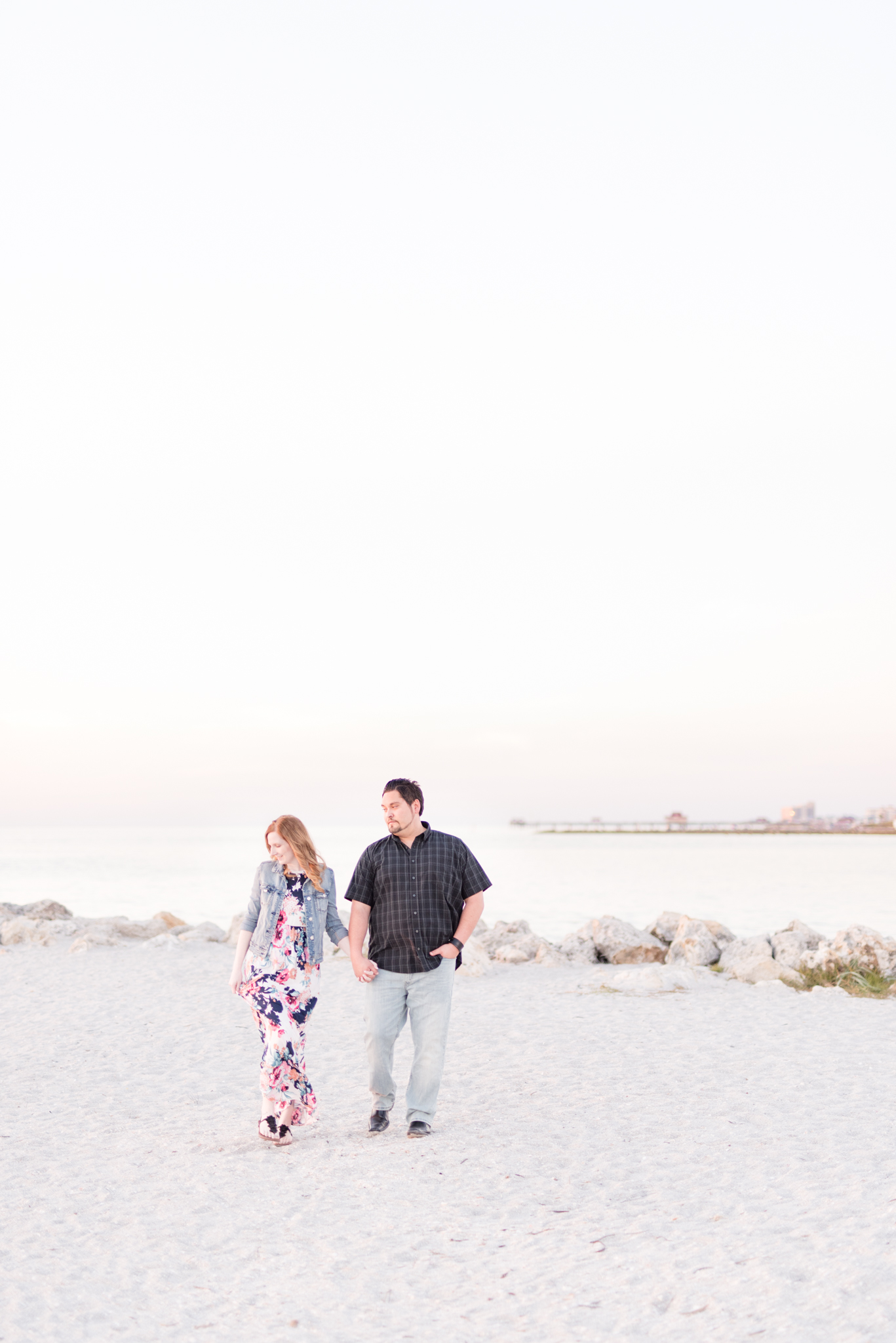 Engaged couple walk along beach at sunset.
