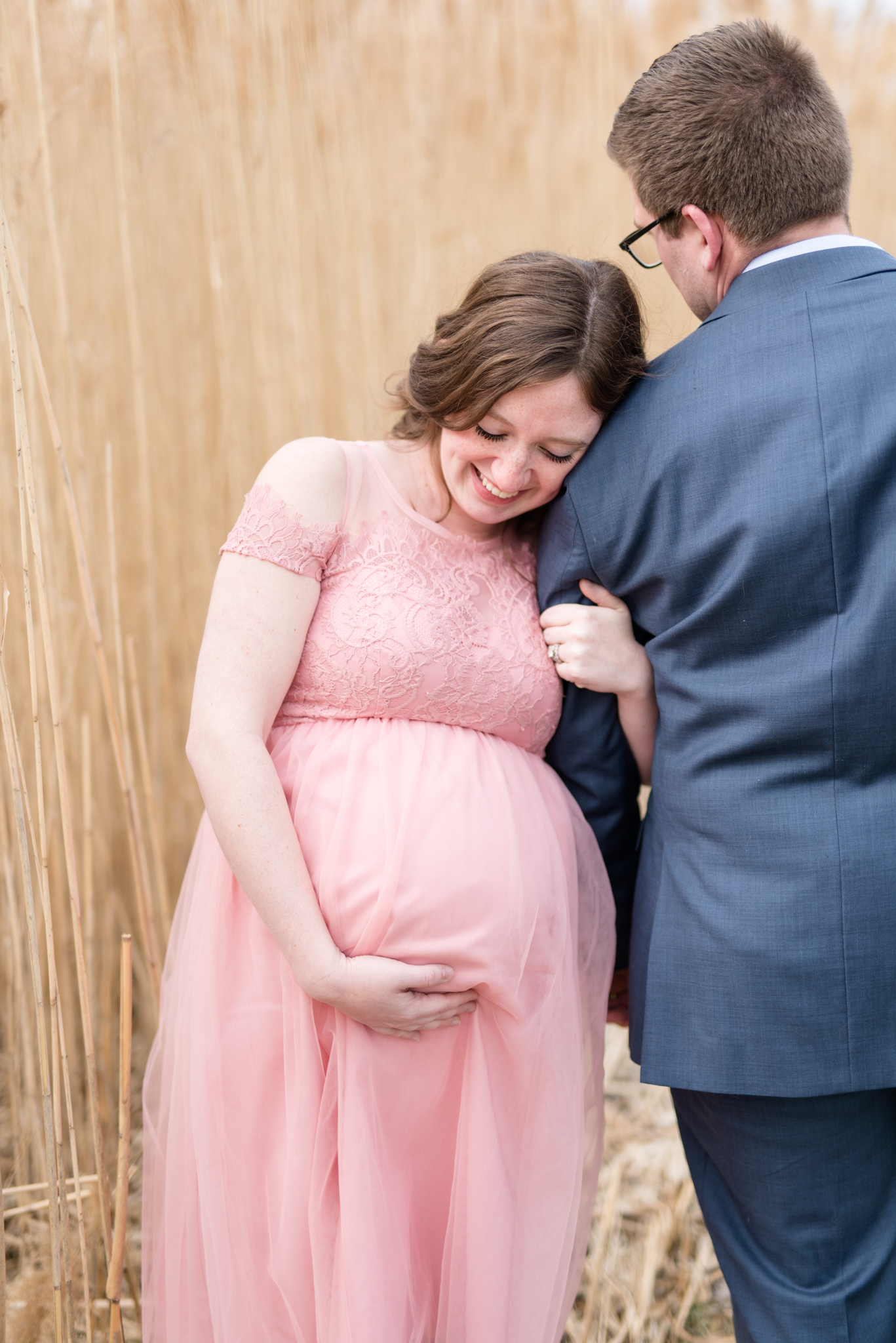 Pregnant mom leans on husband and looks down.