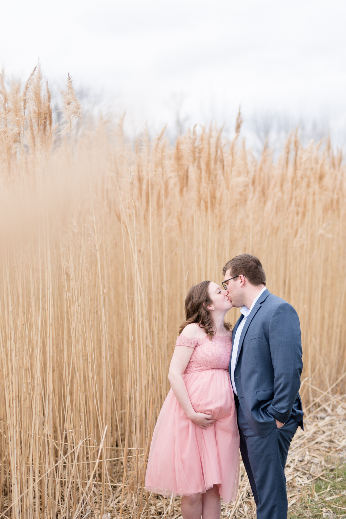 expecting parents kiss in front of wheat field.