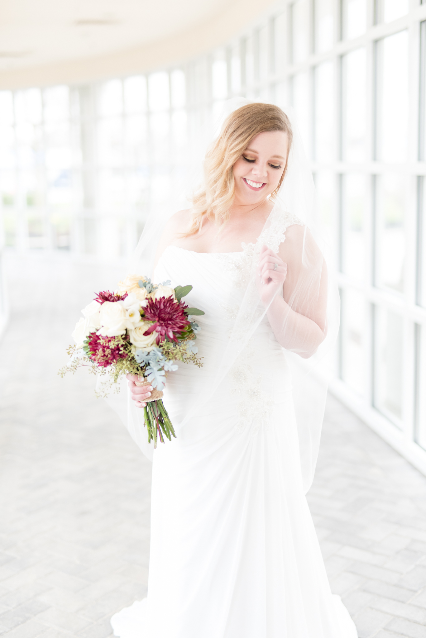 Bride holds onto veil and smiles.