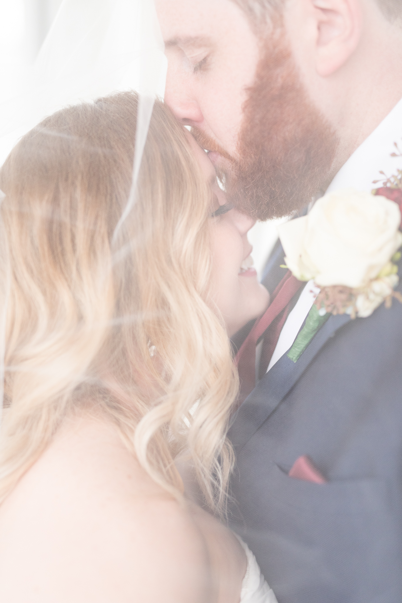 Groom kisses bride's forehead under veil.