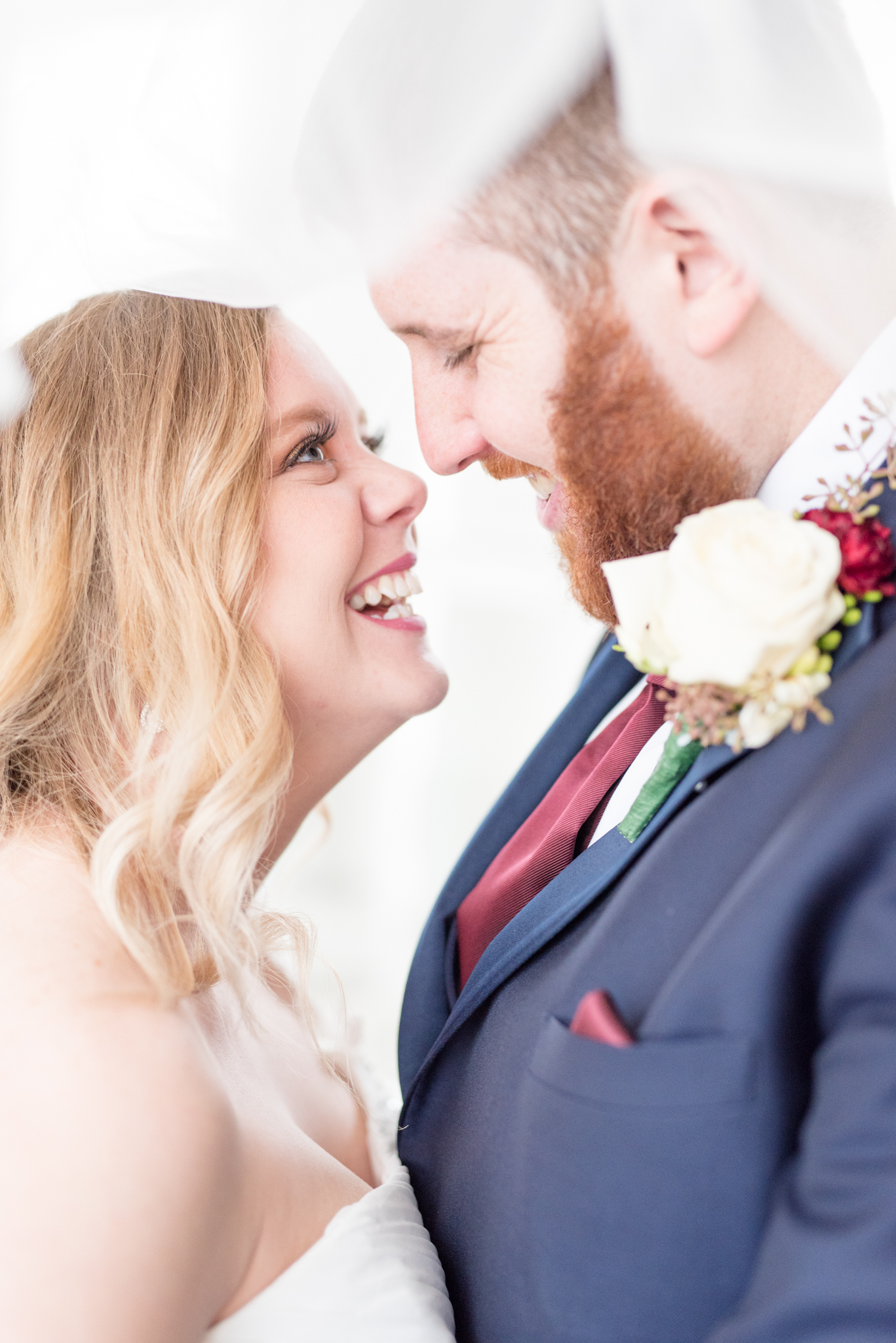 Bride and groom laugh under veil.