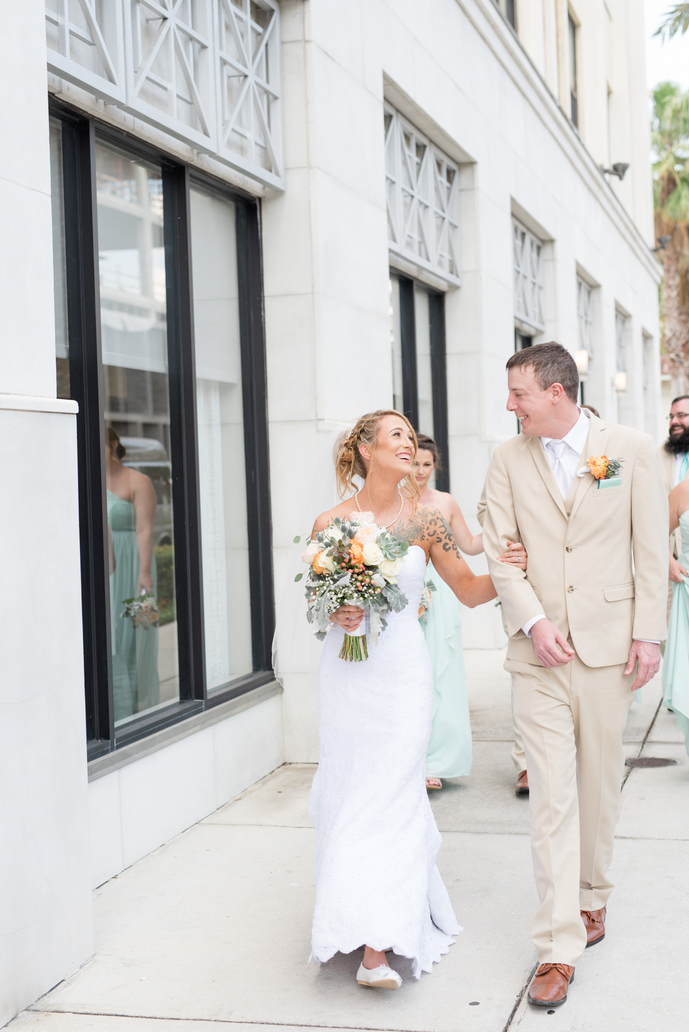 Bride and groom walk down sidewalk with bridal party.