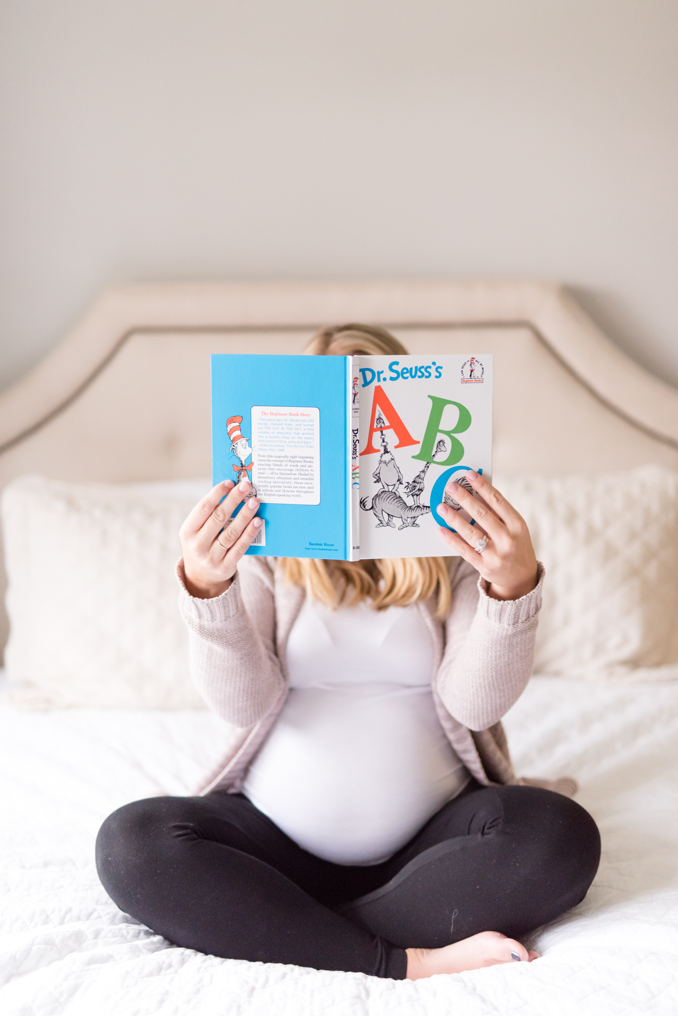 Expecting mother holds book in front of face.