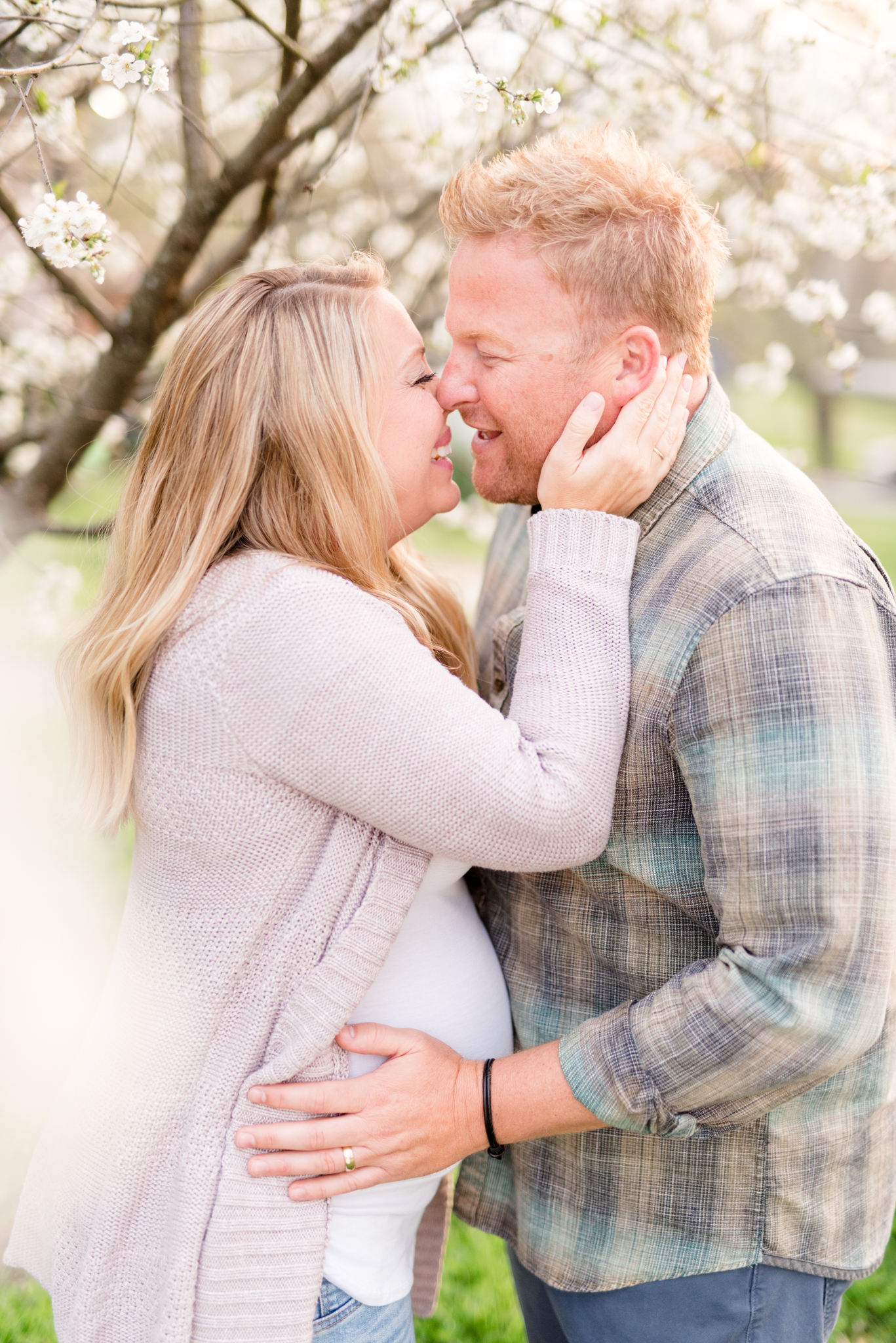 Expecting parents lean in for a kiss under spring blooms.