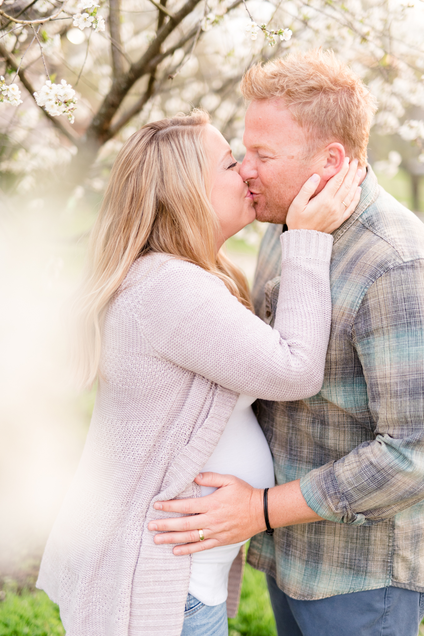 Expecting parents kiss under spring blooms